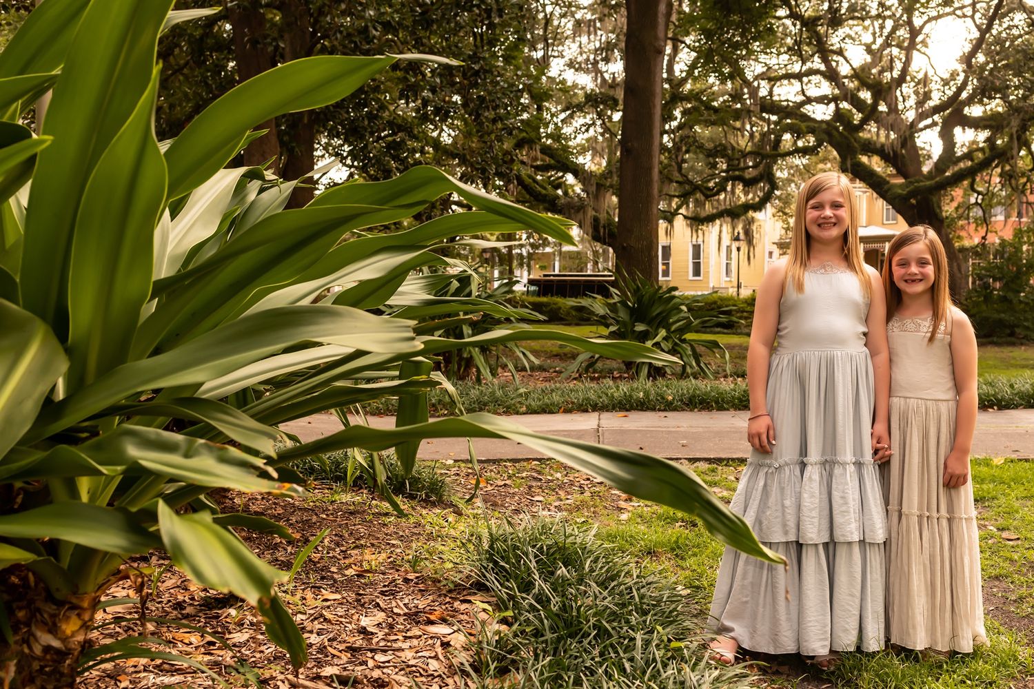 Wedding party stands together in a lush tropical garden setting during golden hour sunlight.