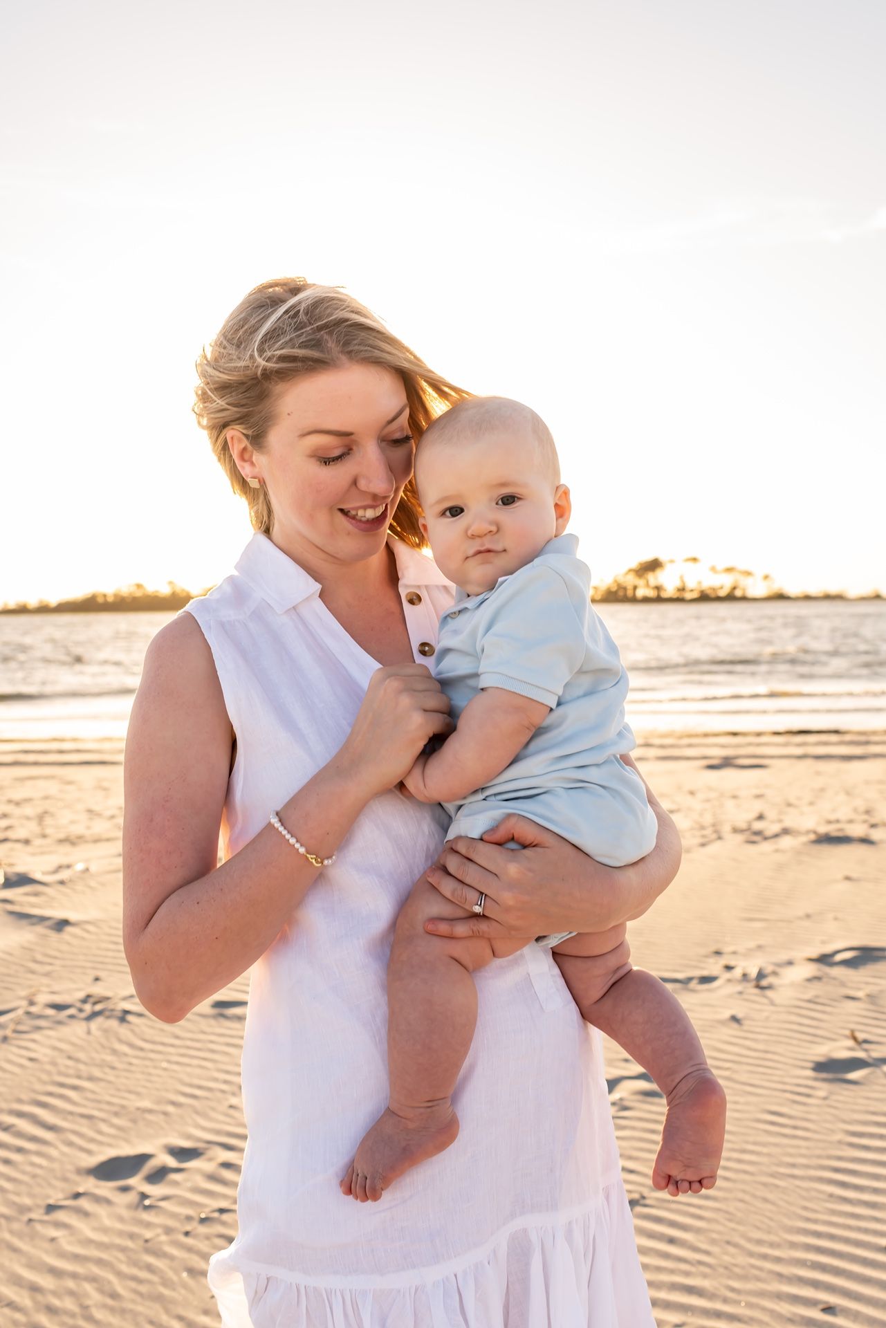 A tender beach photo session shows loving moments with a baby during sunset.