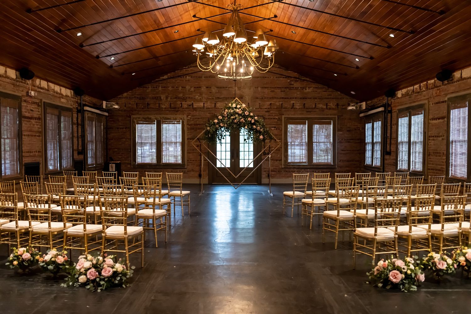 An elegant rustic wedding reception venue with exposed brick walls, chandelier lighting and wooden beams on the ceiling.
