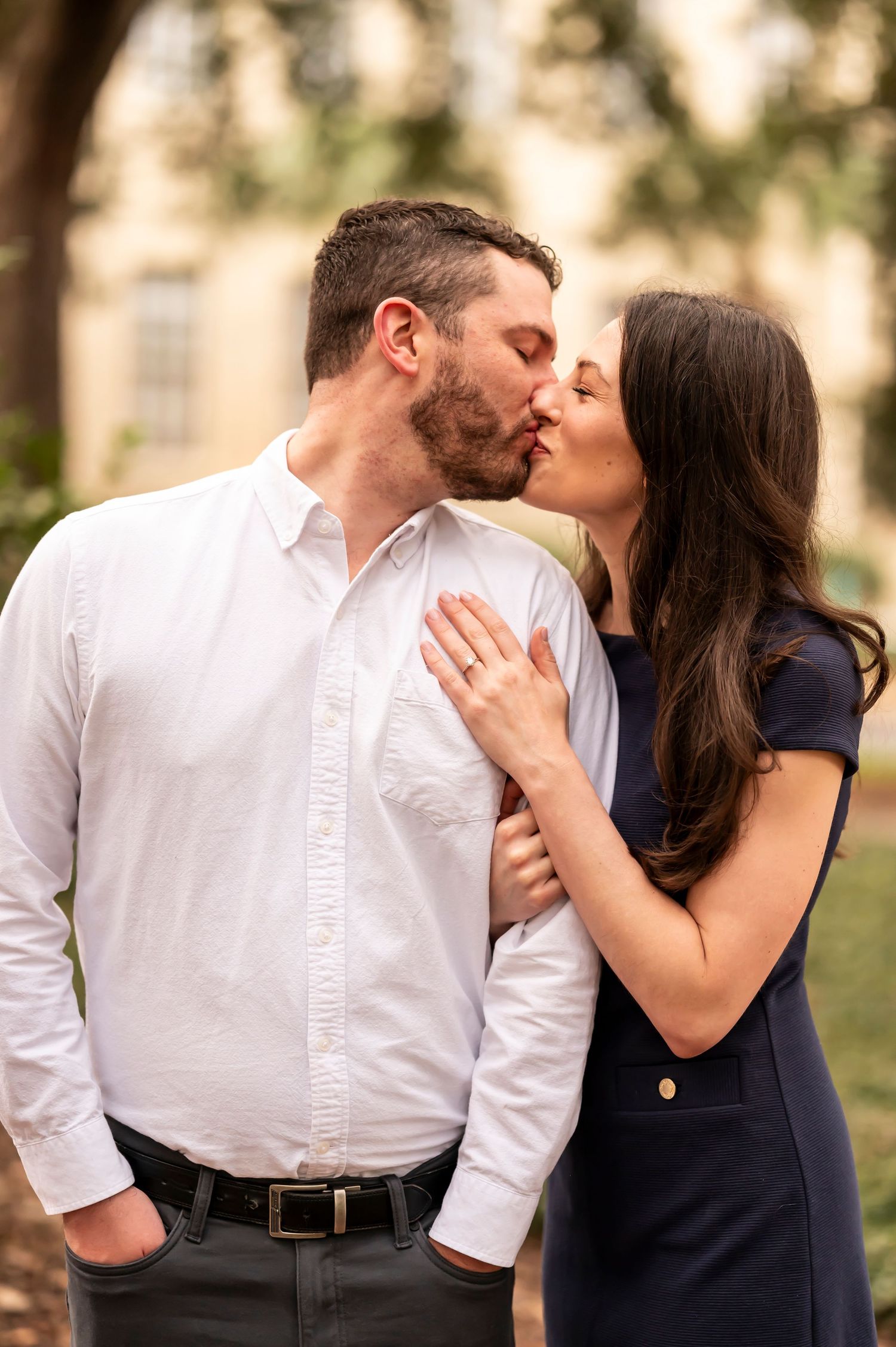 A couple shares a tender kiss outdoors with warm lighting and natural bokeh background.
