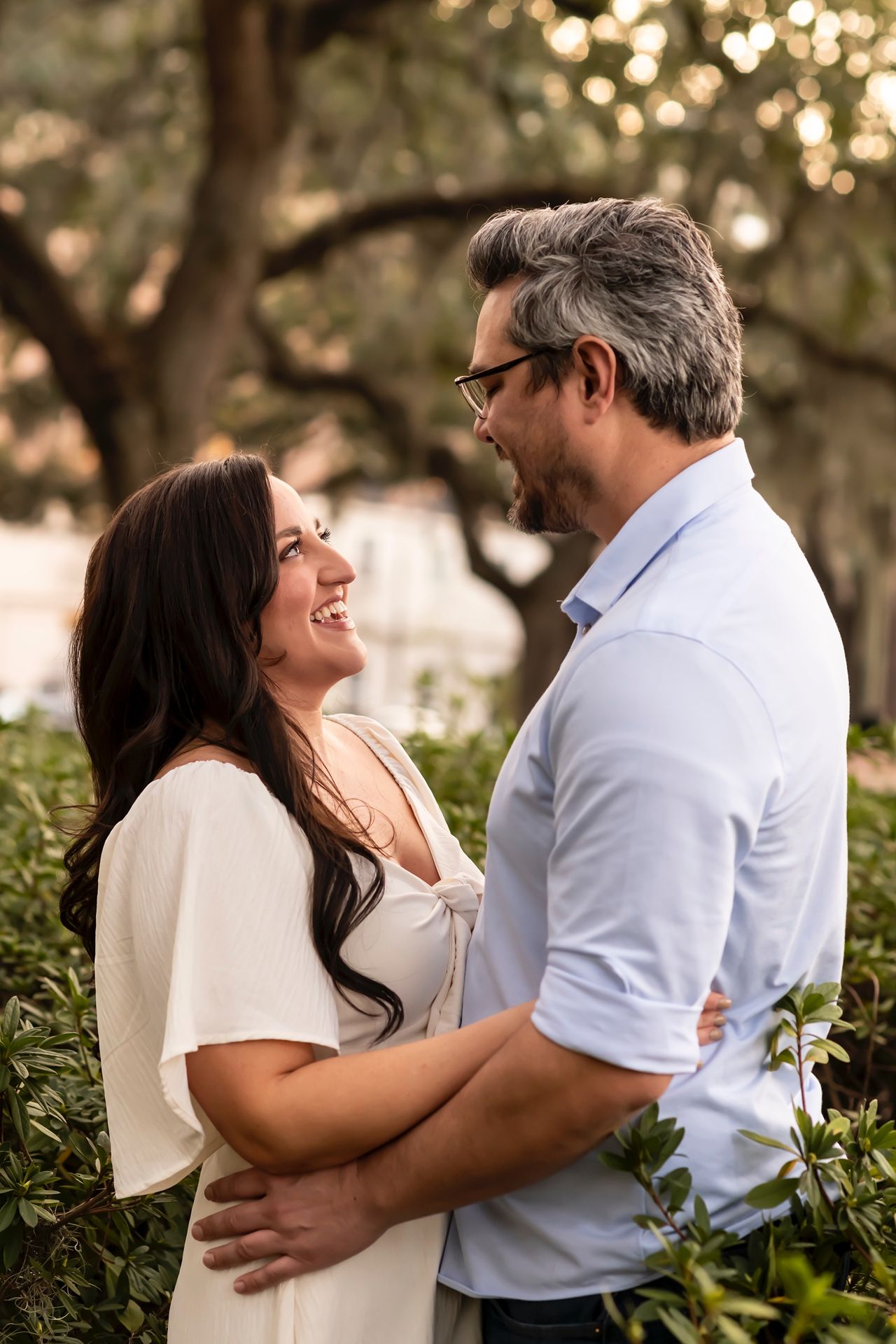 Romantic couple embraces in outdoor garden setting with soft bokeh lights and greenery in background.