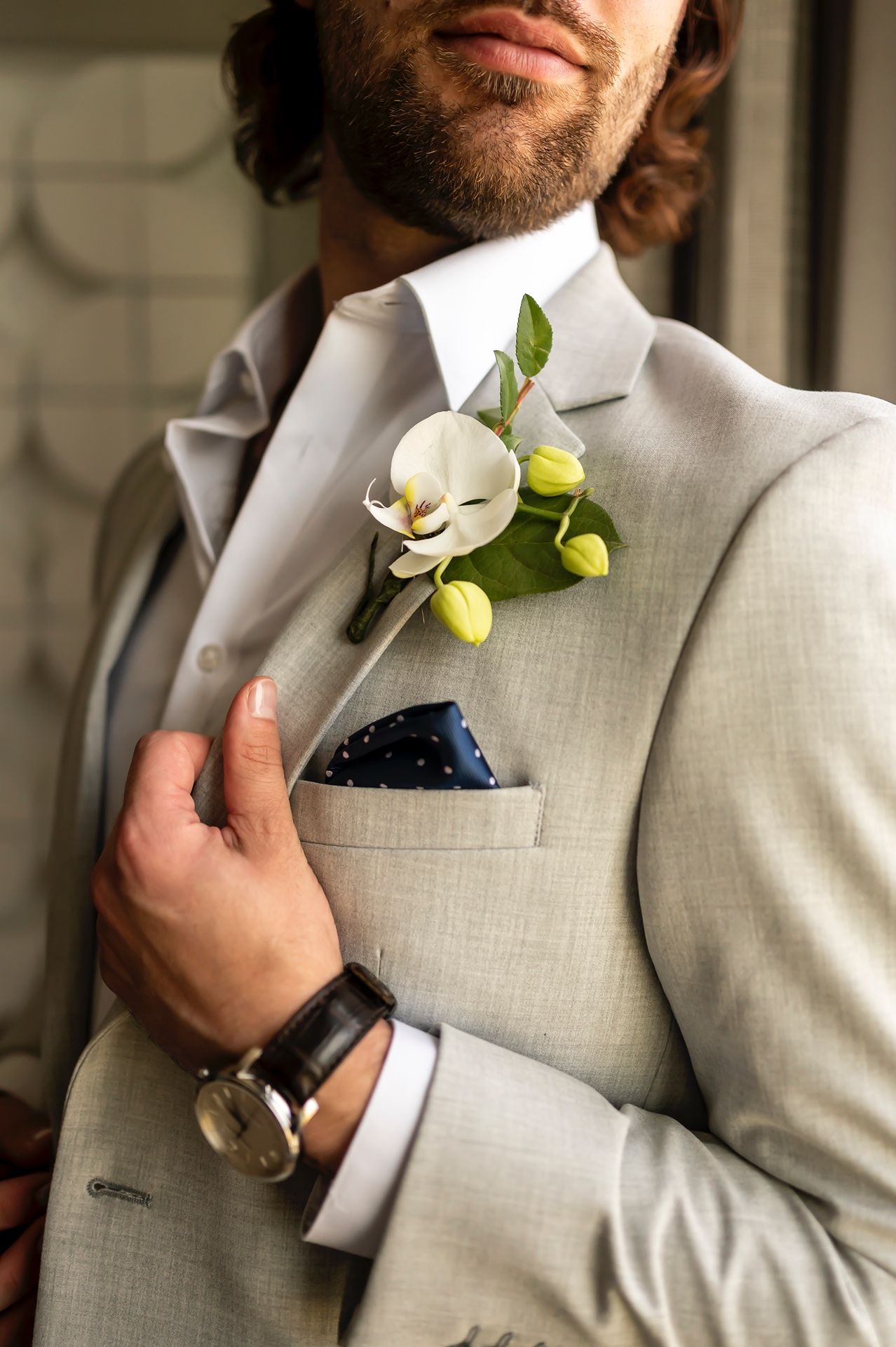 A close-up of a light grey suit jacket with a white orchid boutonniere featuring lime green accents in the pocket.