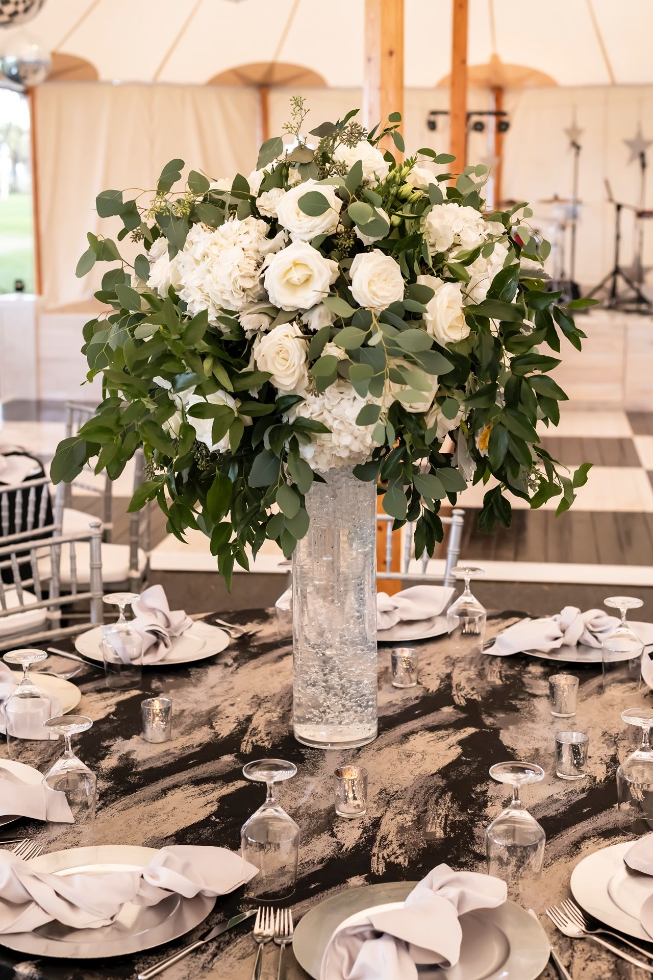 Elegant wedding reception table decor with white roses and eucalyptus centerpieces atop driftwood pieces and crystal vases.