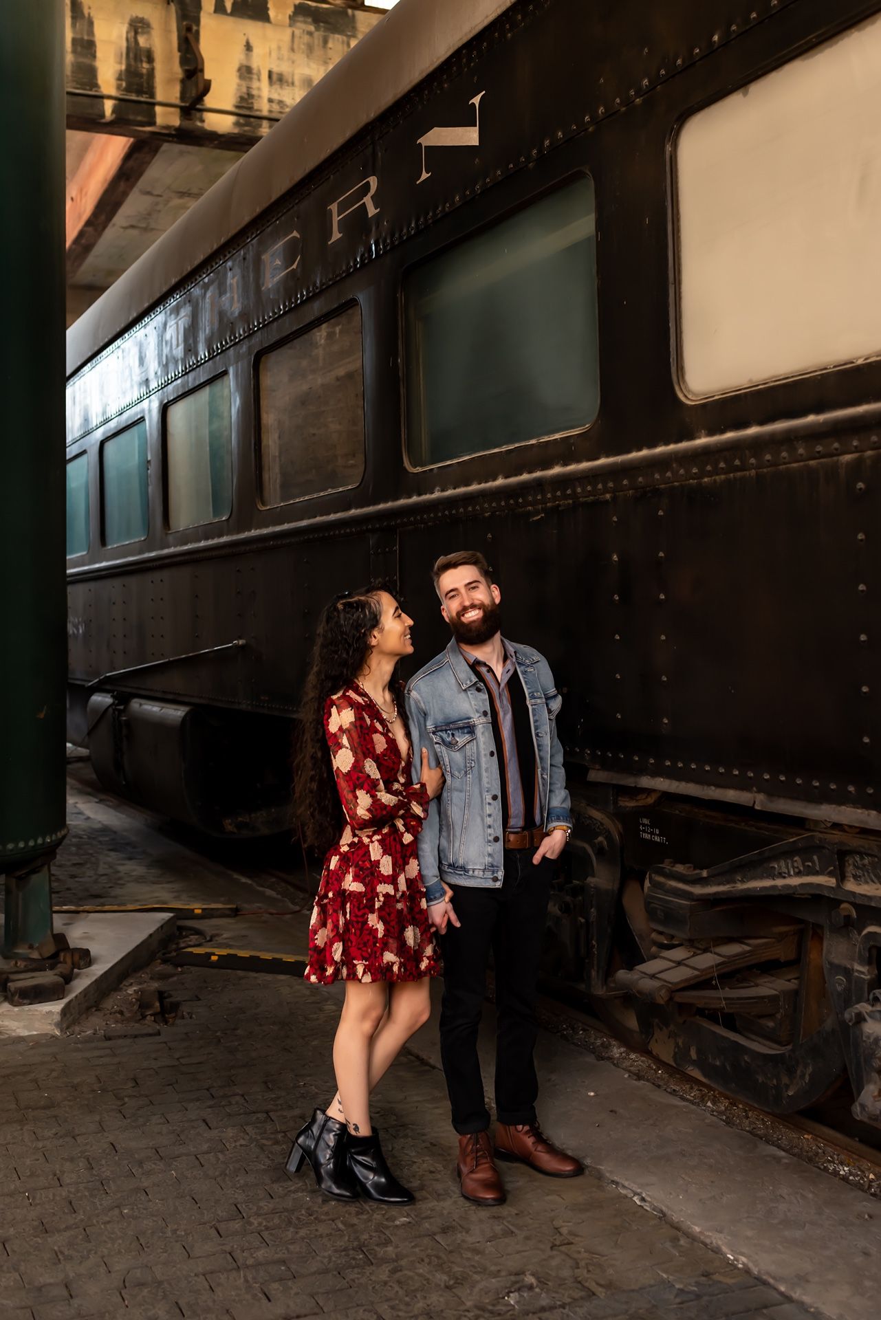 Couple poses in romantic sequence against dark vintage train car during atmospheric engagement photo shoot.