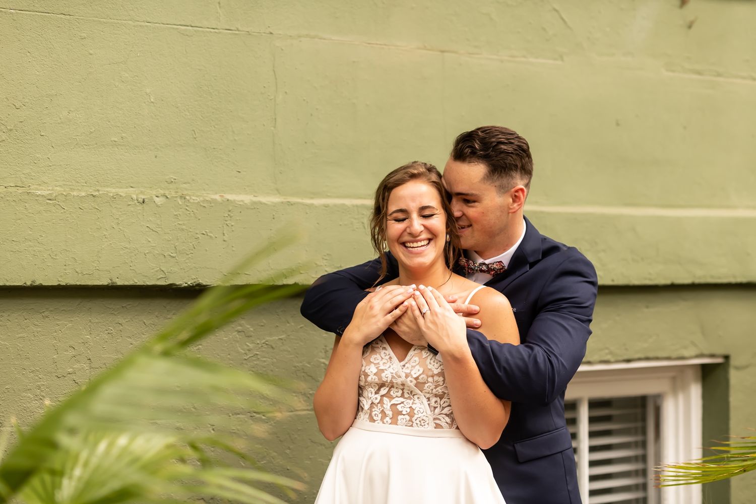 A romantic moment between a couple embracing outdoors with the bride wearing a sparkly white gown against a green wall.