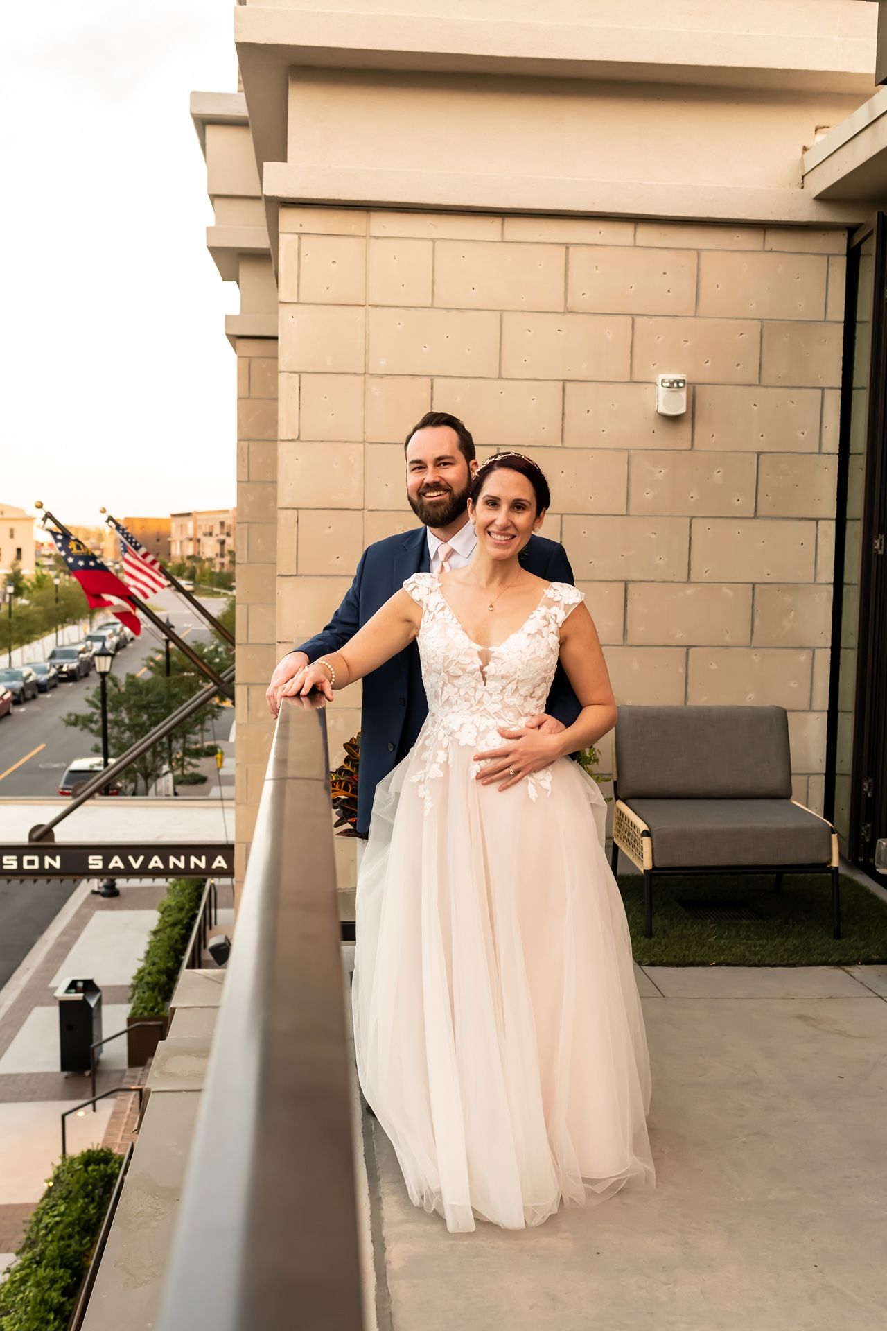 Newlyweds pose together on outdoor balcony of modern building during sunset.