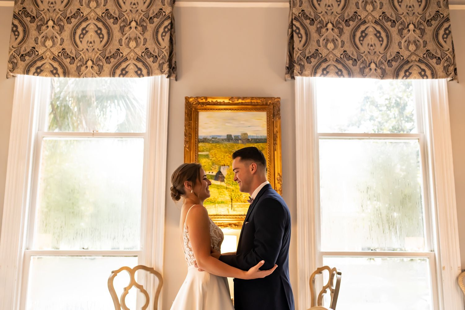 Ornate interior room with multiple windows, antique wallpaper, and framed artwork in an elegant historic setting.