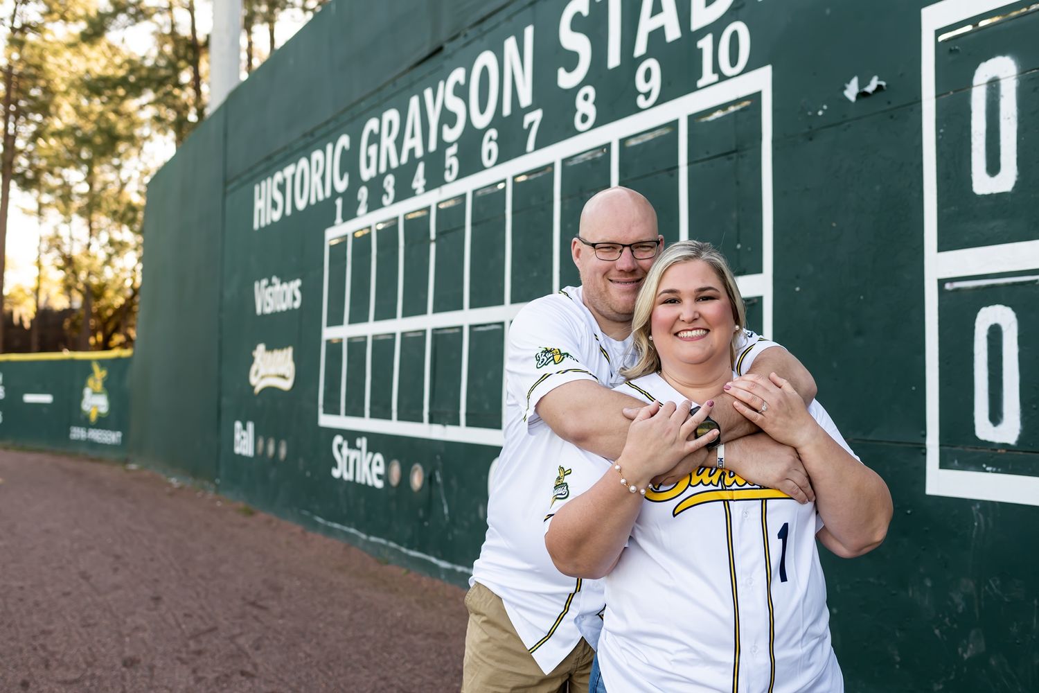 A happy couple celebrates their graduation from Michigan State University at a stadium with green boards in view.
