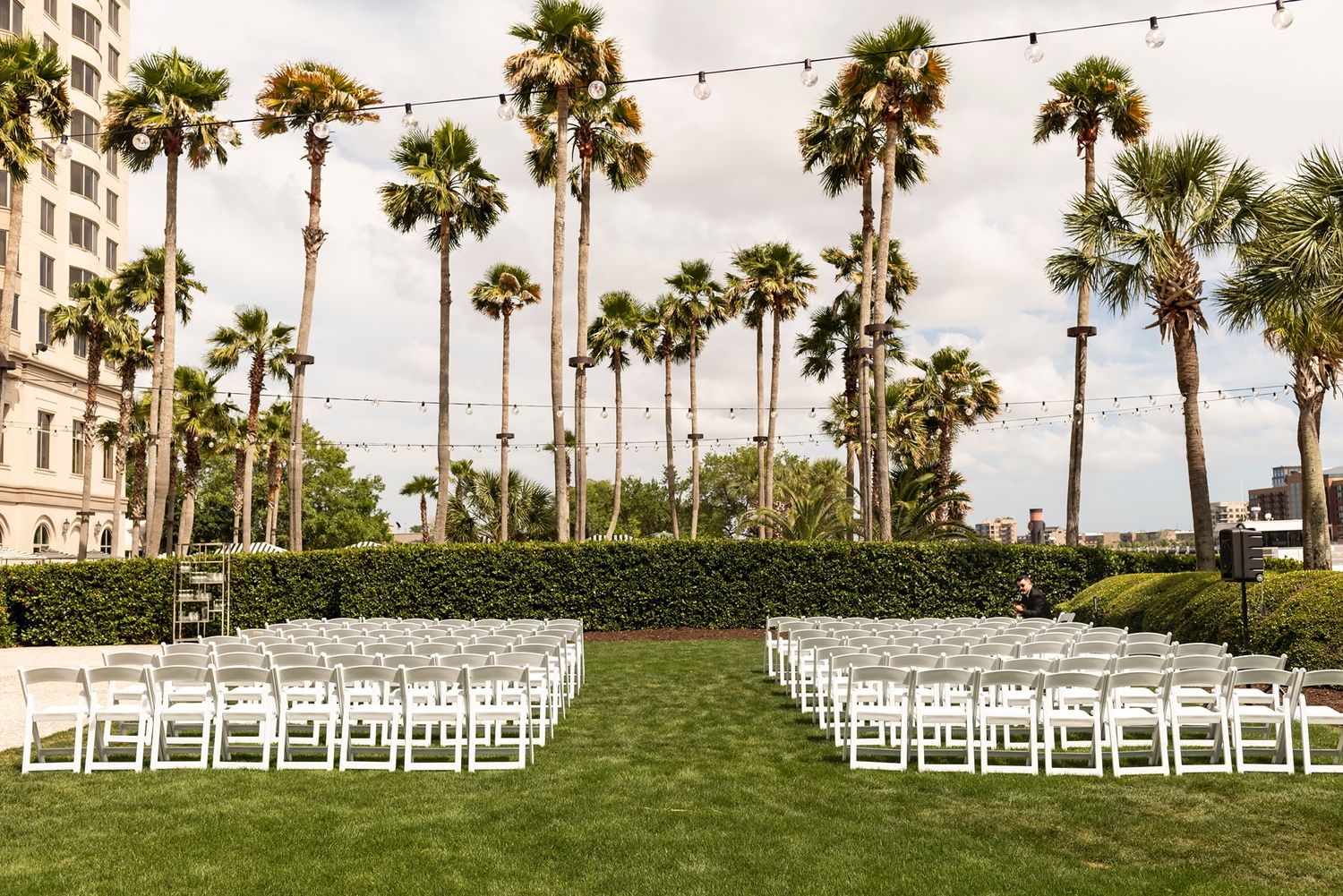 Wedding ceremony setup with white chairs lined up facing a waterfront view with palm trees.