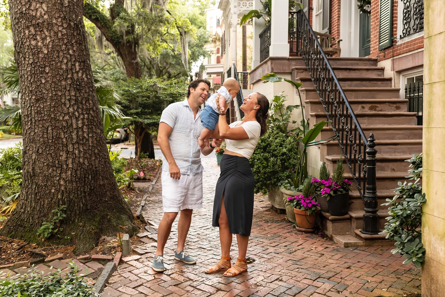 Two people share a tender moment under a large tree in a historic garden setting.