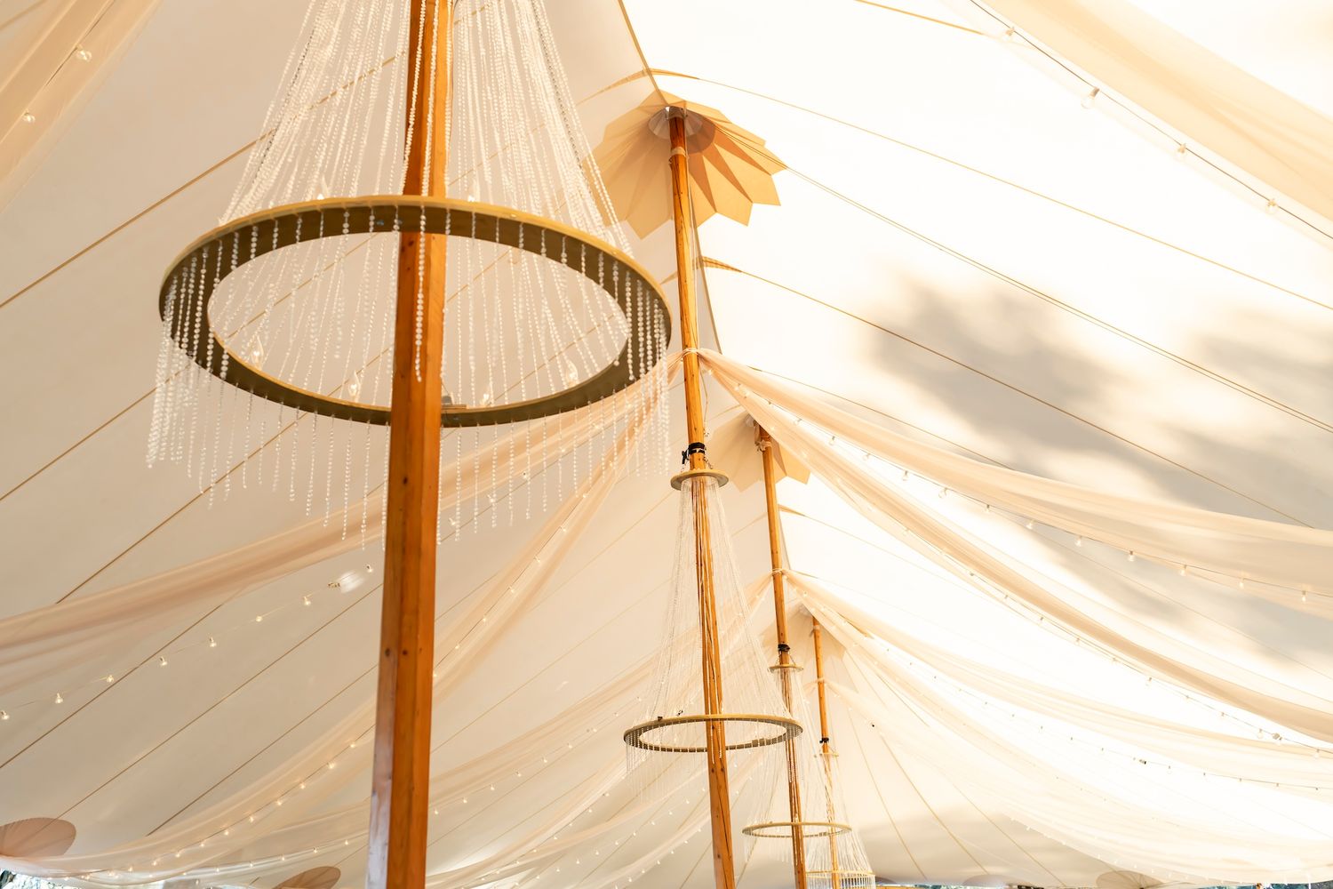 Looking up at circular chandelier light fixtures hanging from tent poles under white draped fabric ceiling.