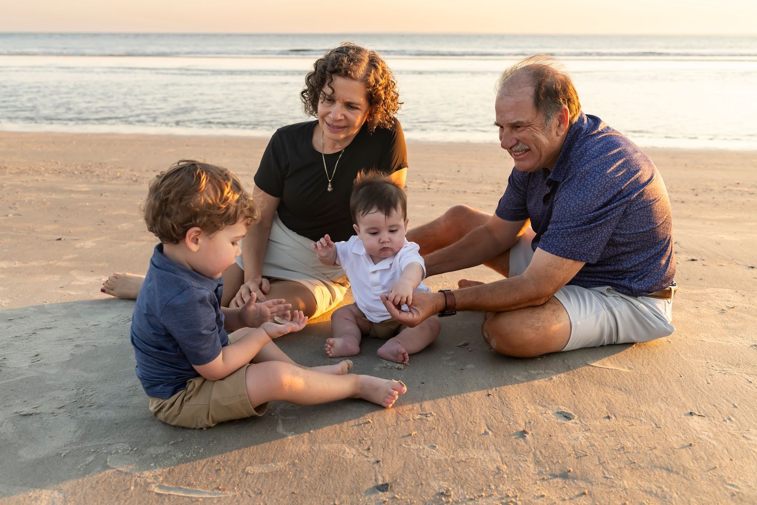 Group enjoying family playtime together on a sandy beach at sunset.