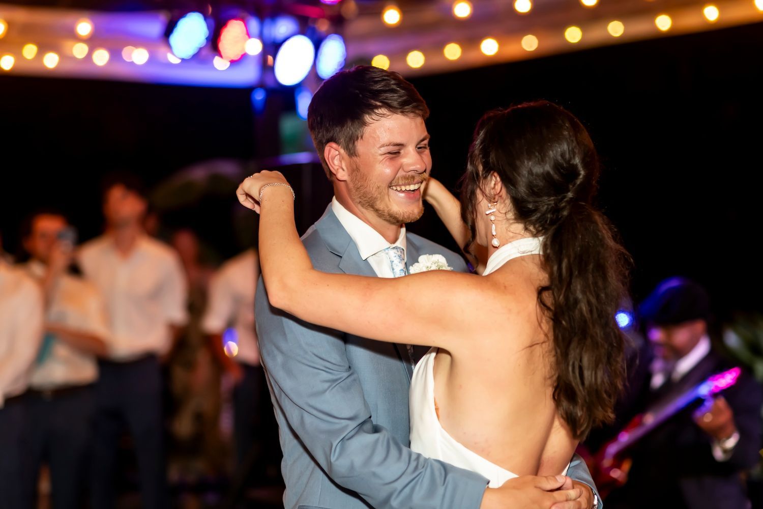 A couple shares a joyful dance moment at a reception with twinkling lights and bokeh in the background.