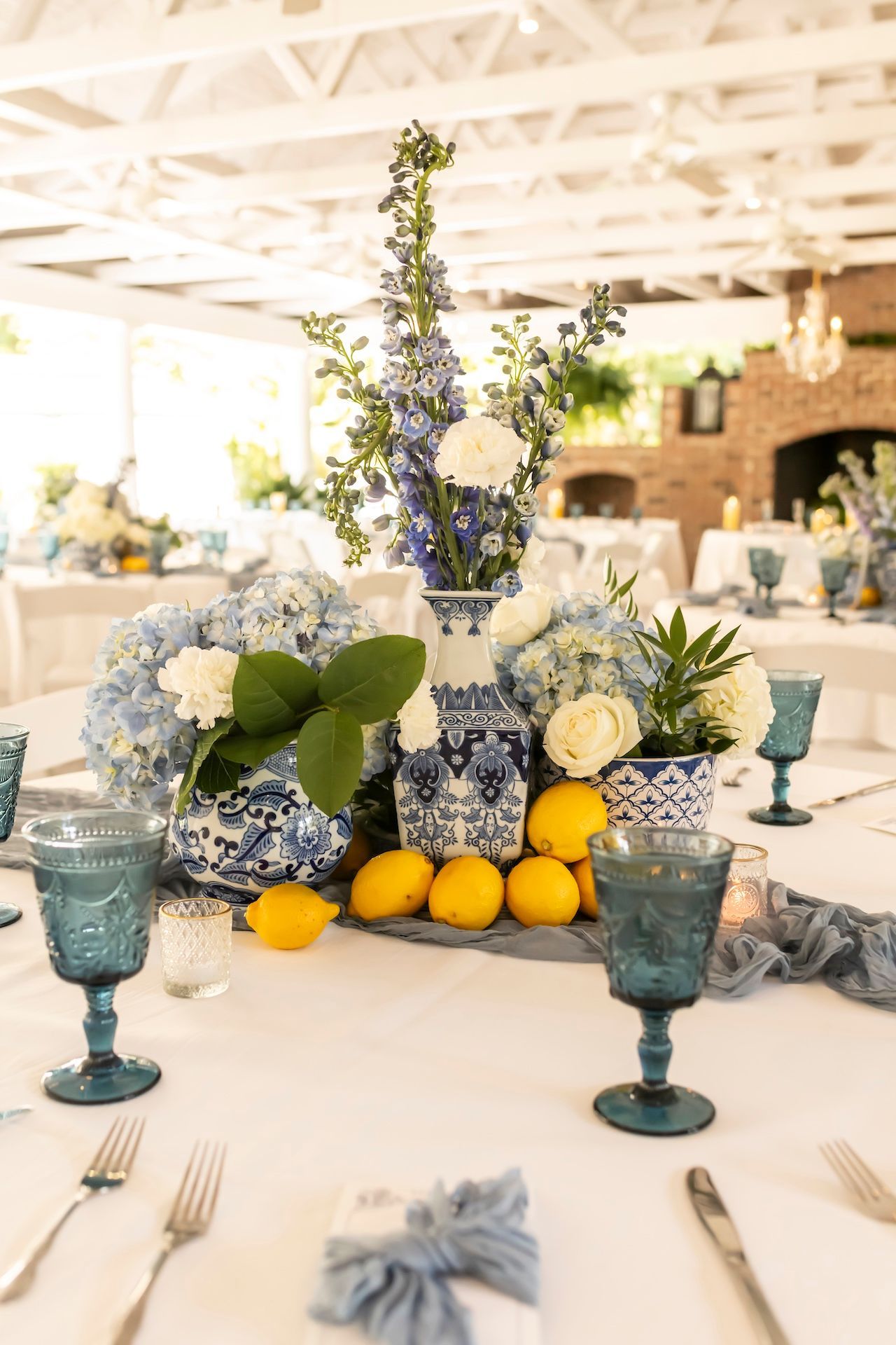 Wedding table centerpiece with blue and white hydrangeas, fresh lemons, and blue glassware in elegant chinoiserie vases.