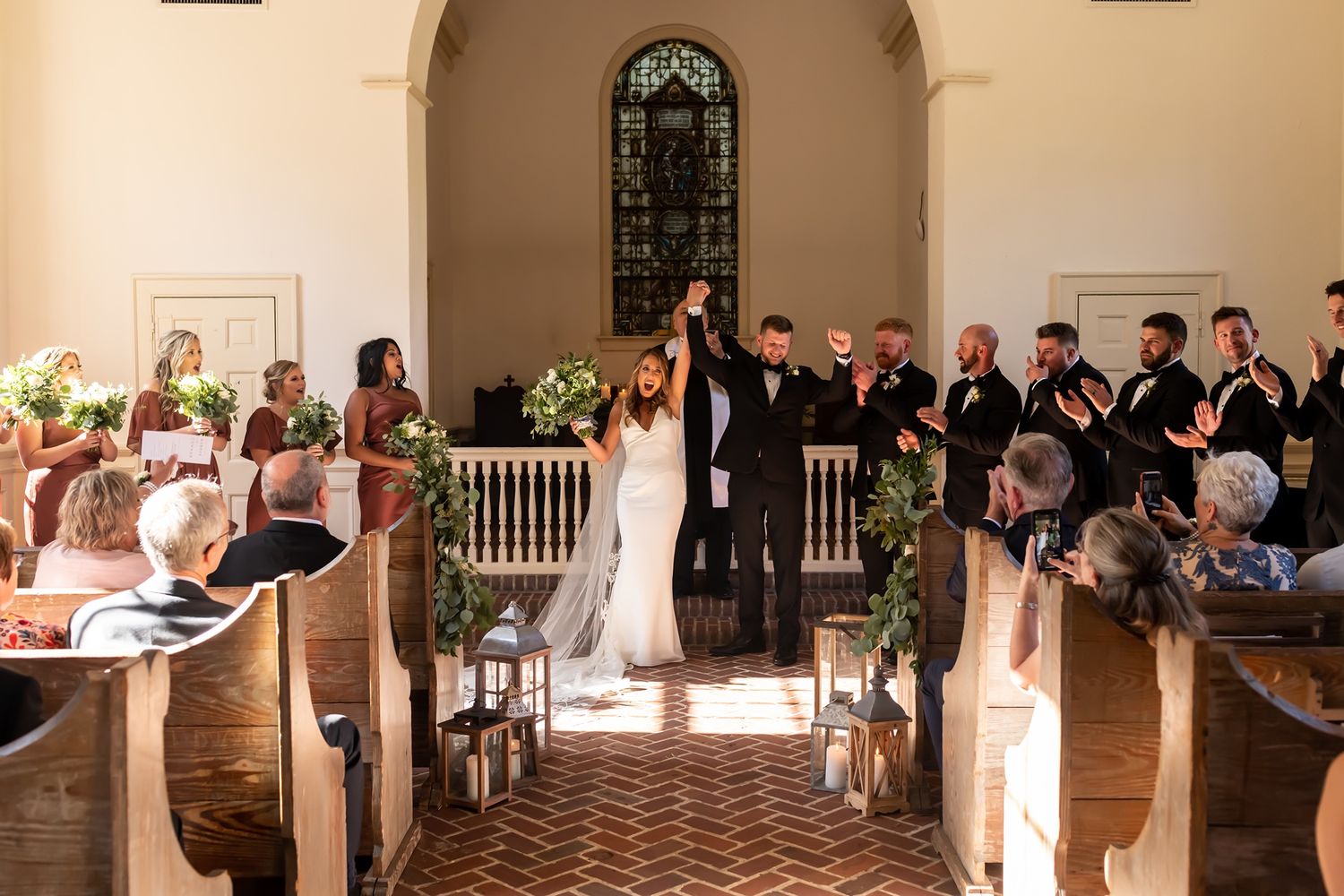 Wedding guests gather on an elegant wraparound porch of a stately white home during an evening celebration.