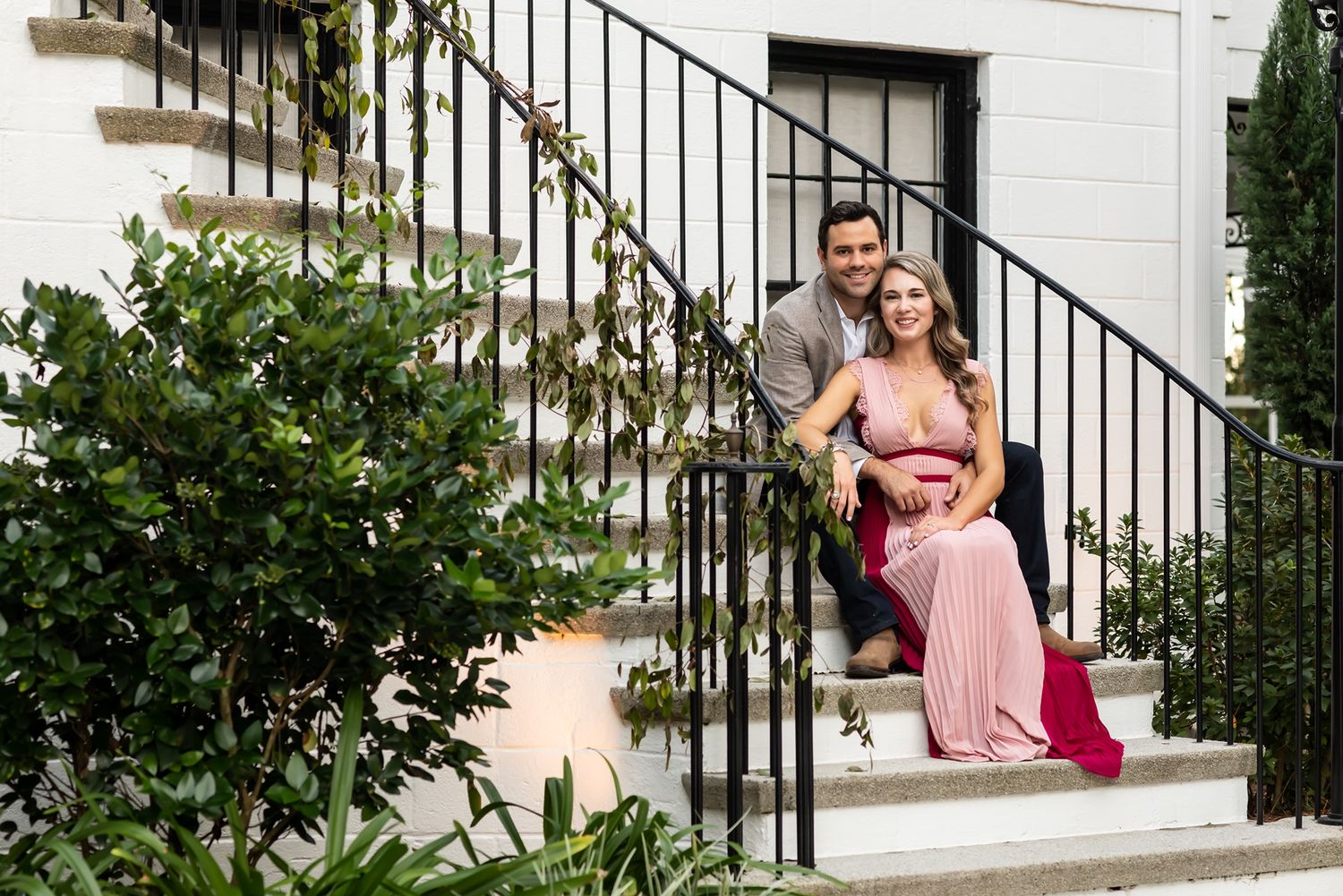Elegant outdoor photoshoot by white stairs and iron railing surrounded by lush greenery.