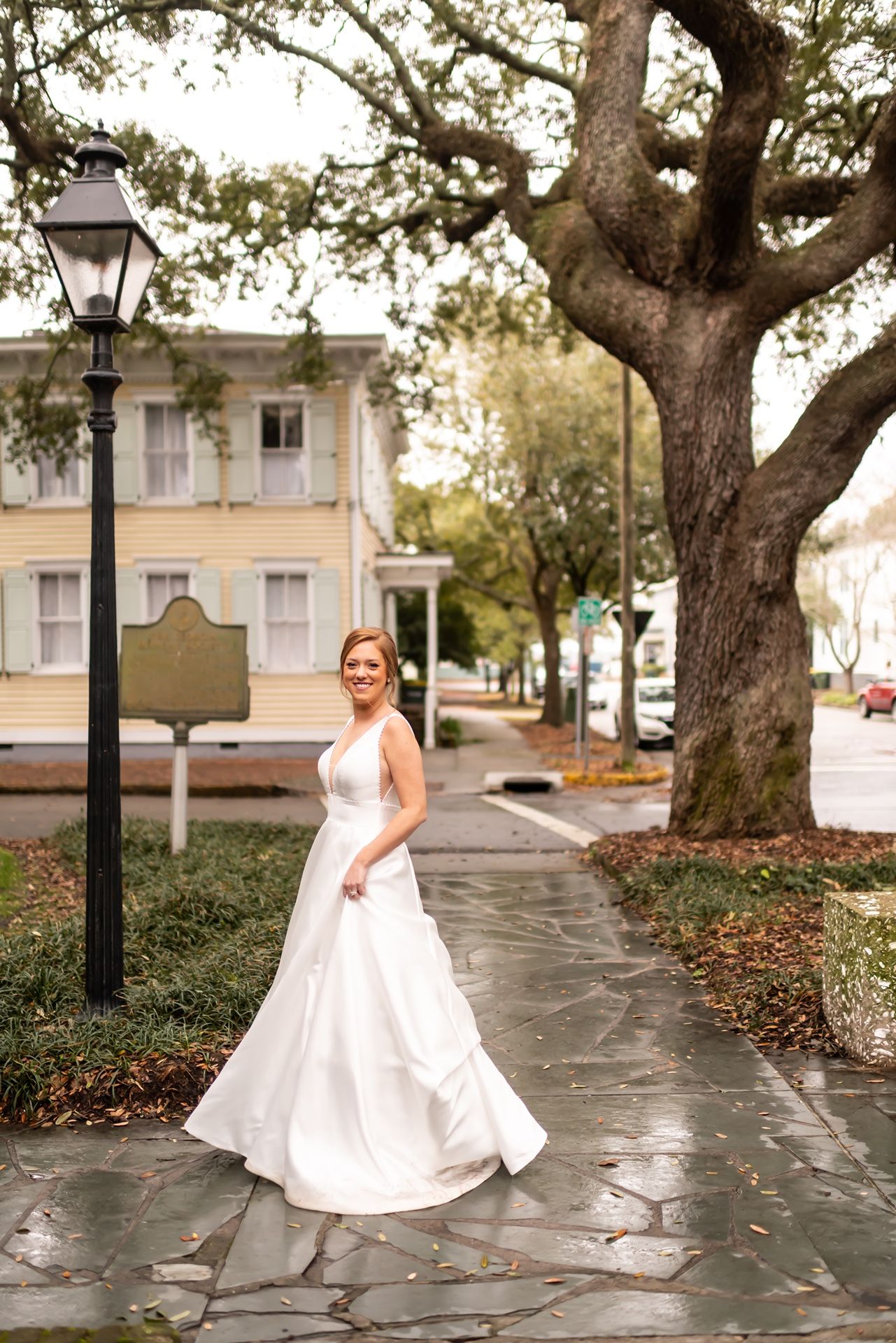 A wedding photograph series showing a person in a white bridal gown standing on a stone path under large oak trees.