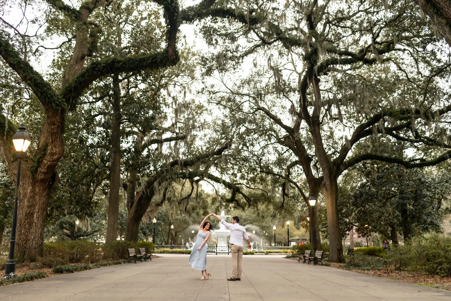 Couple holds hands walking through a moss-draped oak tree lined path in Forsyth Park, Savannah, Georgia.
