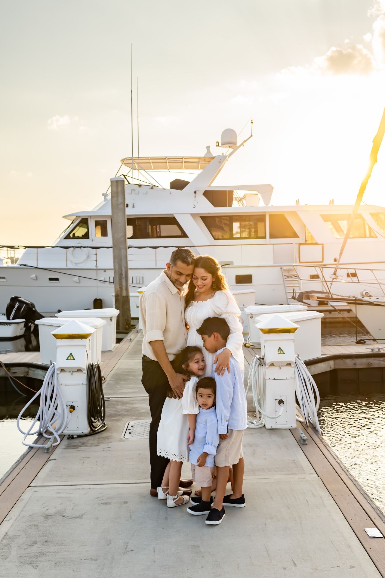 Family of five poses on a marina dock at golden hour with a white yacht in the background.