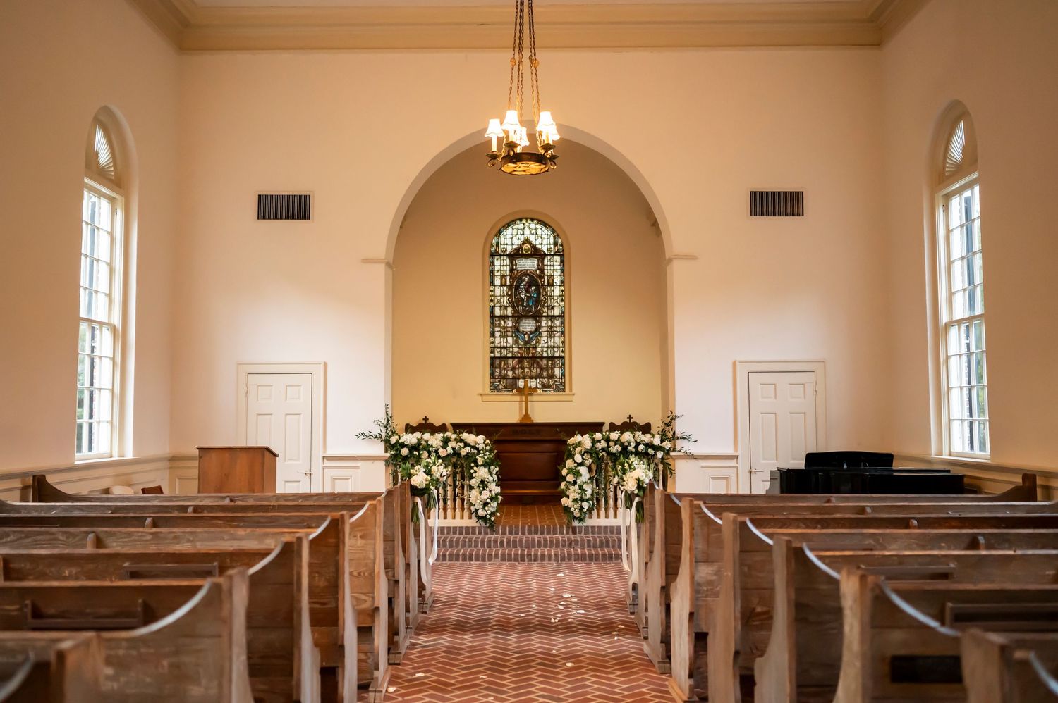 A traditional church chapel interior with wooden pews, arched windows, and crown molding illuminated by warm lighting.