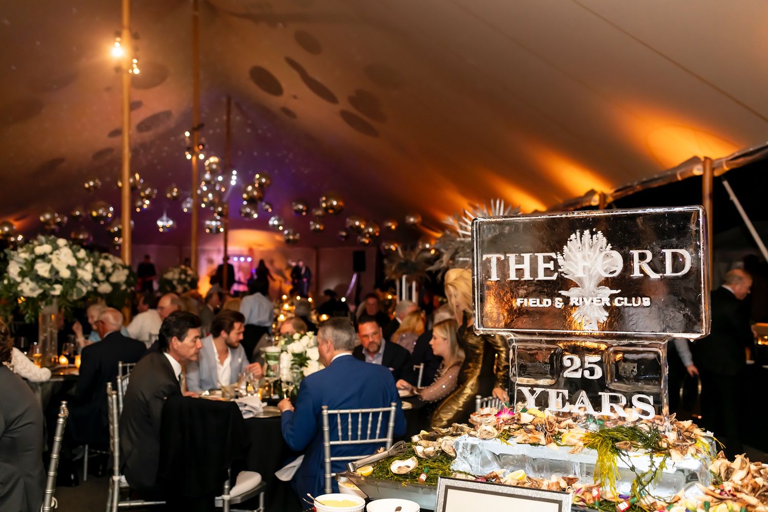 Elegant evening celebration under a tent with elegant table settings, glowing lights and a custom event sign for The FRD.