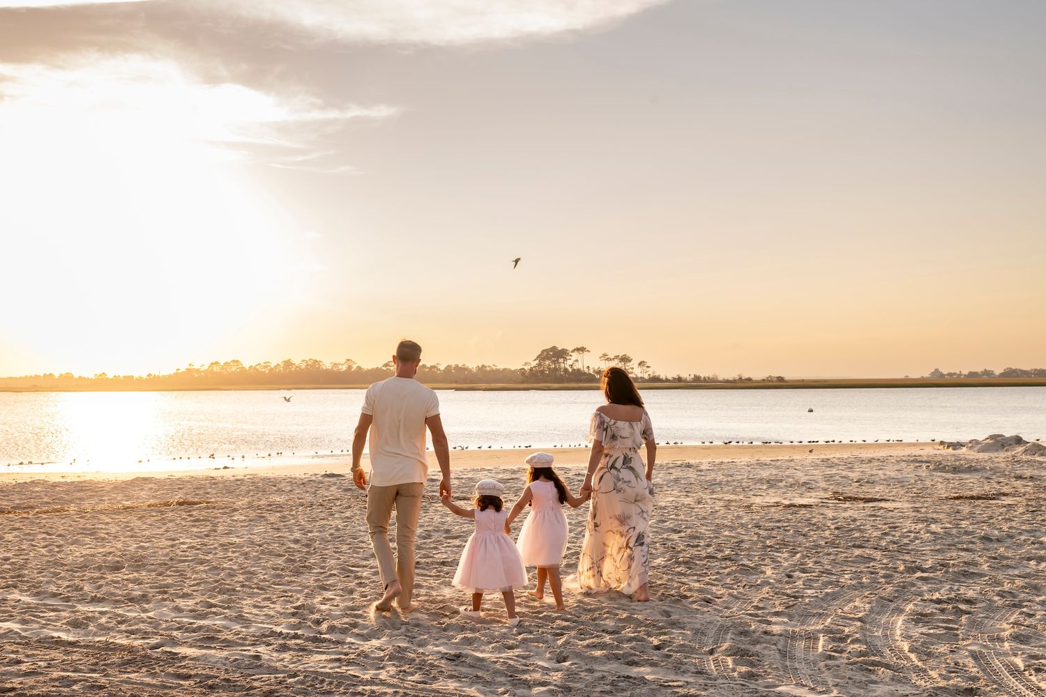 Family walking on beach at sunset holding hands, silhouetted against golden sky and ocean.