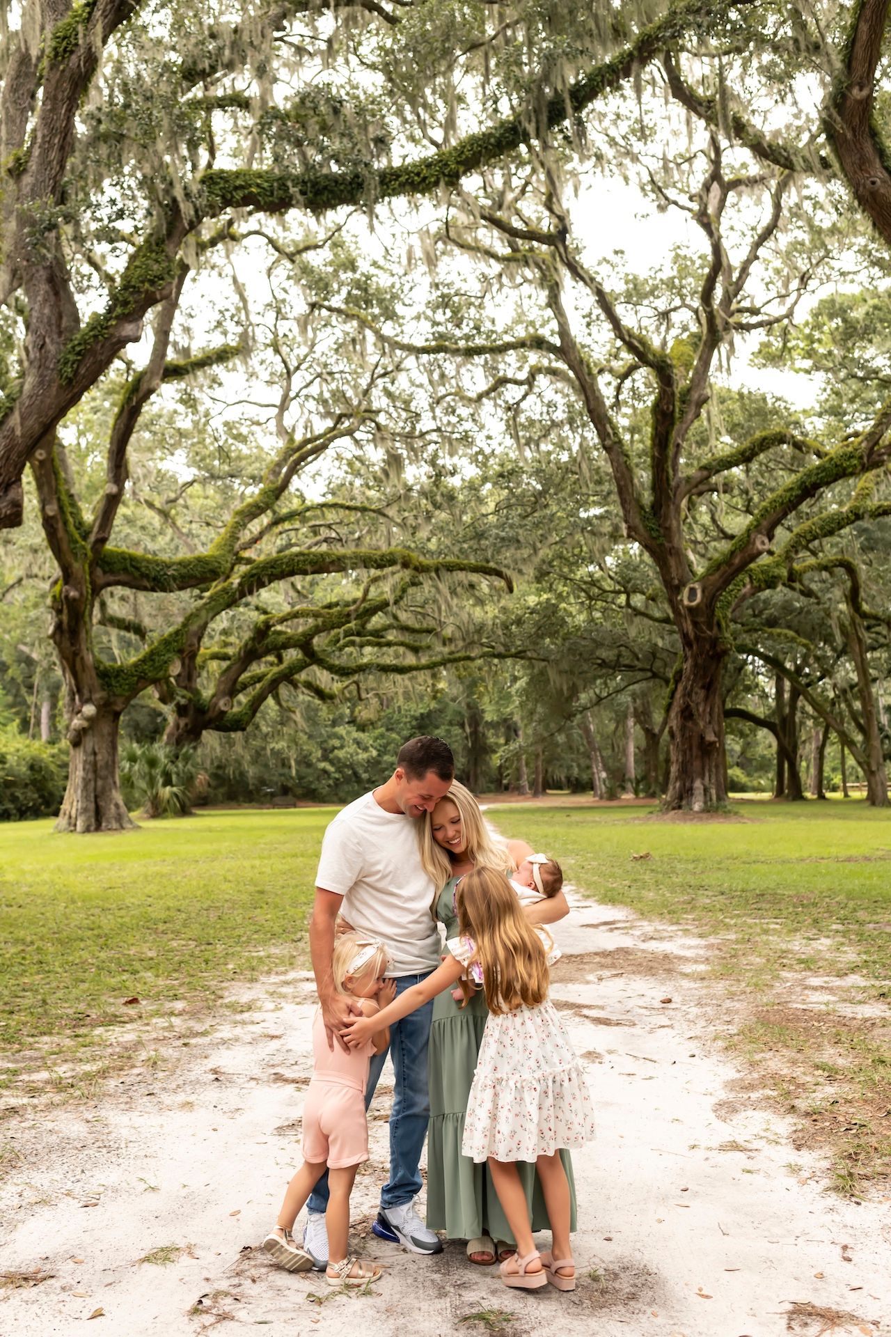 A loving family shares a tender moment together on a sandy path under majestic oak trees draped with Spanish moss.