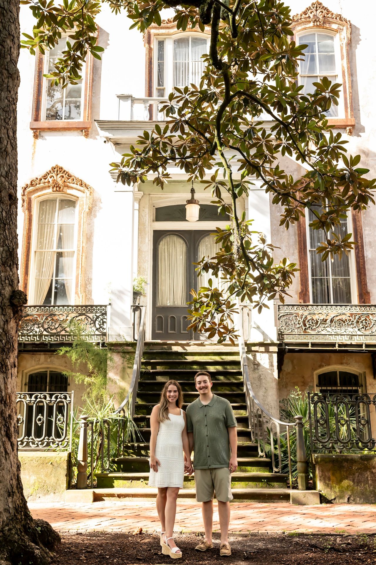 Historic ornate white building with tall windows and decorative details framed by magnolia branches in Savannah, Georgia.