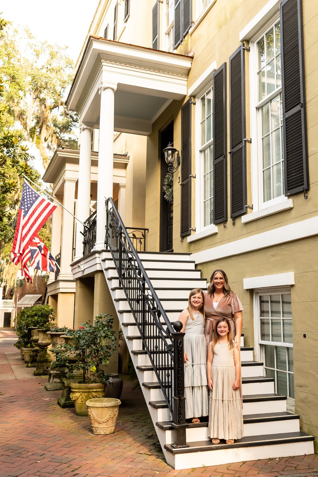 A celebration outside a cream-colored historic home with black shutters and American flags on display.