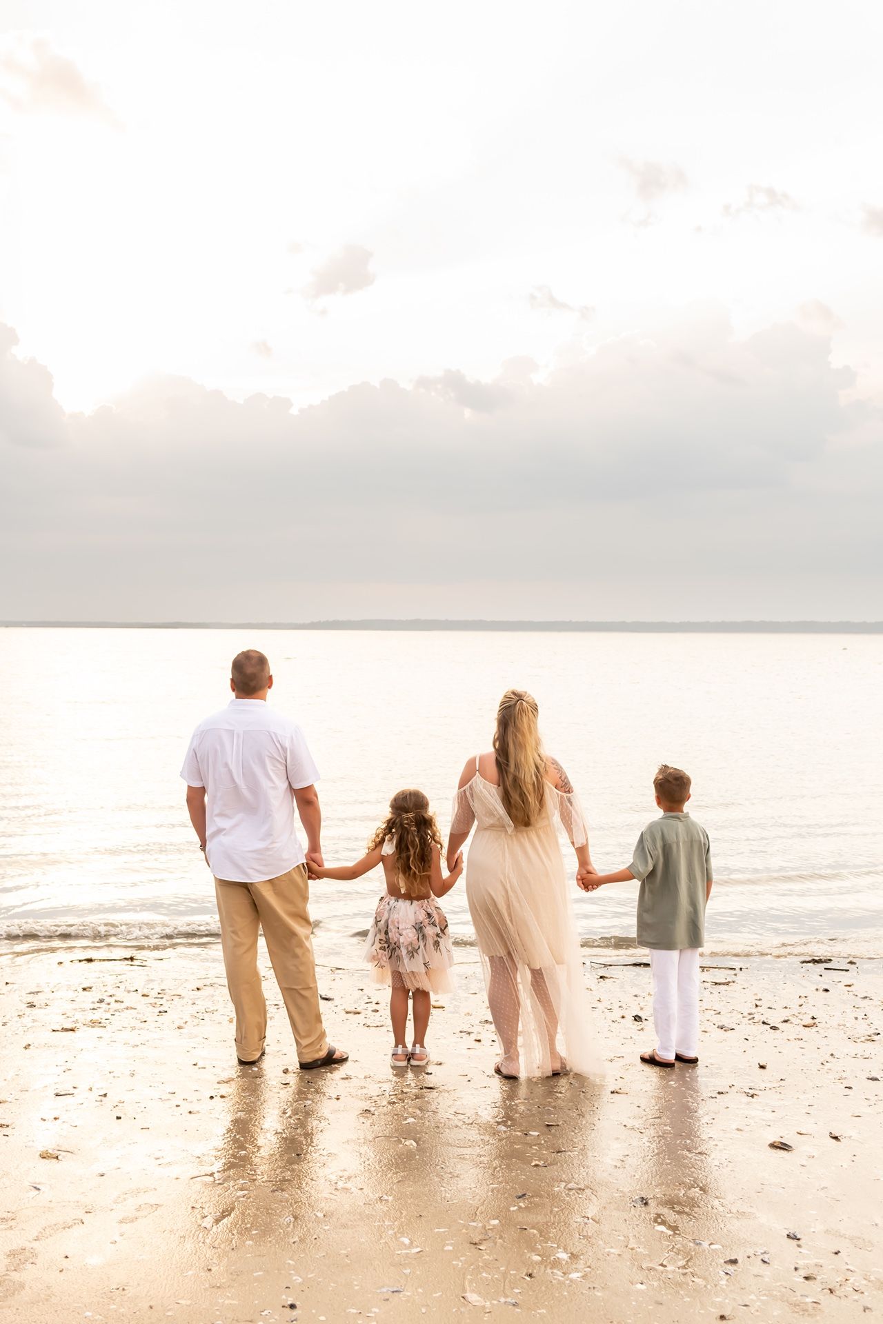 A family holds hands while walking together along a peaceful beach at sunset.