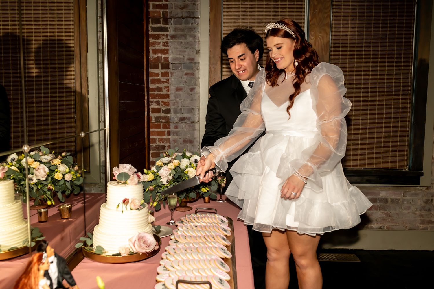 A couple in formal wedding attire cuts their tiered white wedding cake together at their reception.