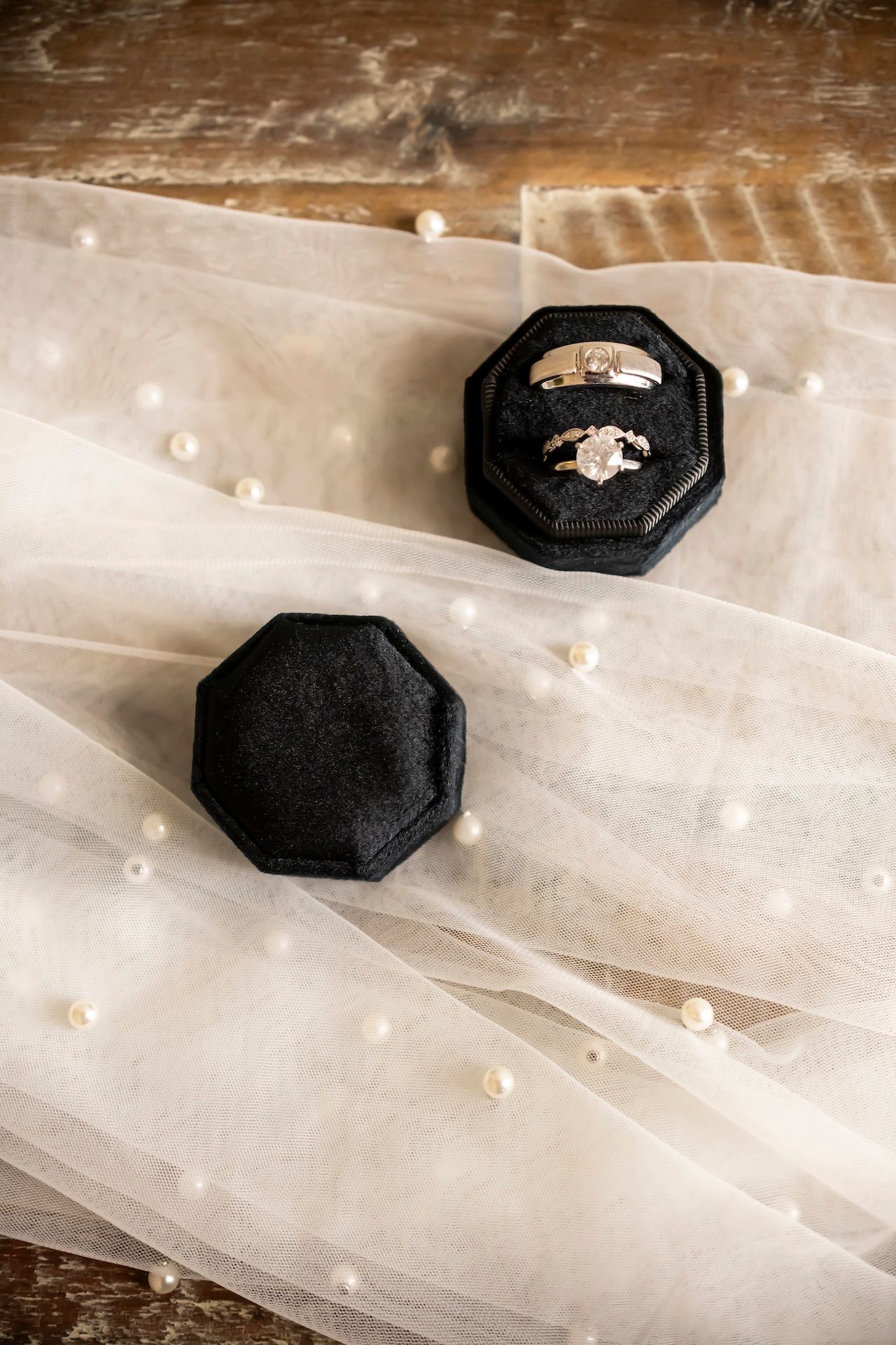 An engagement ring in a black octagonal box sits atop delicate sheer fabric with pearl embellishments.