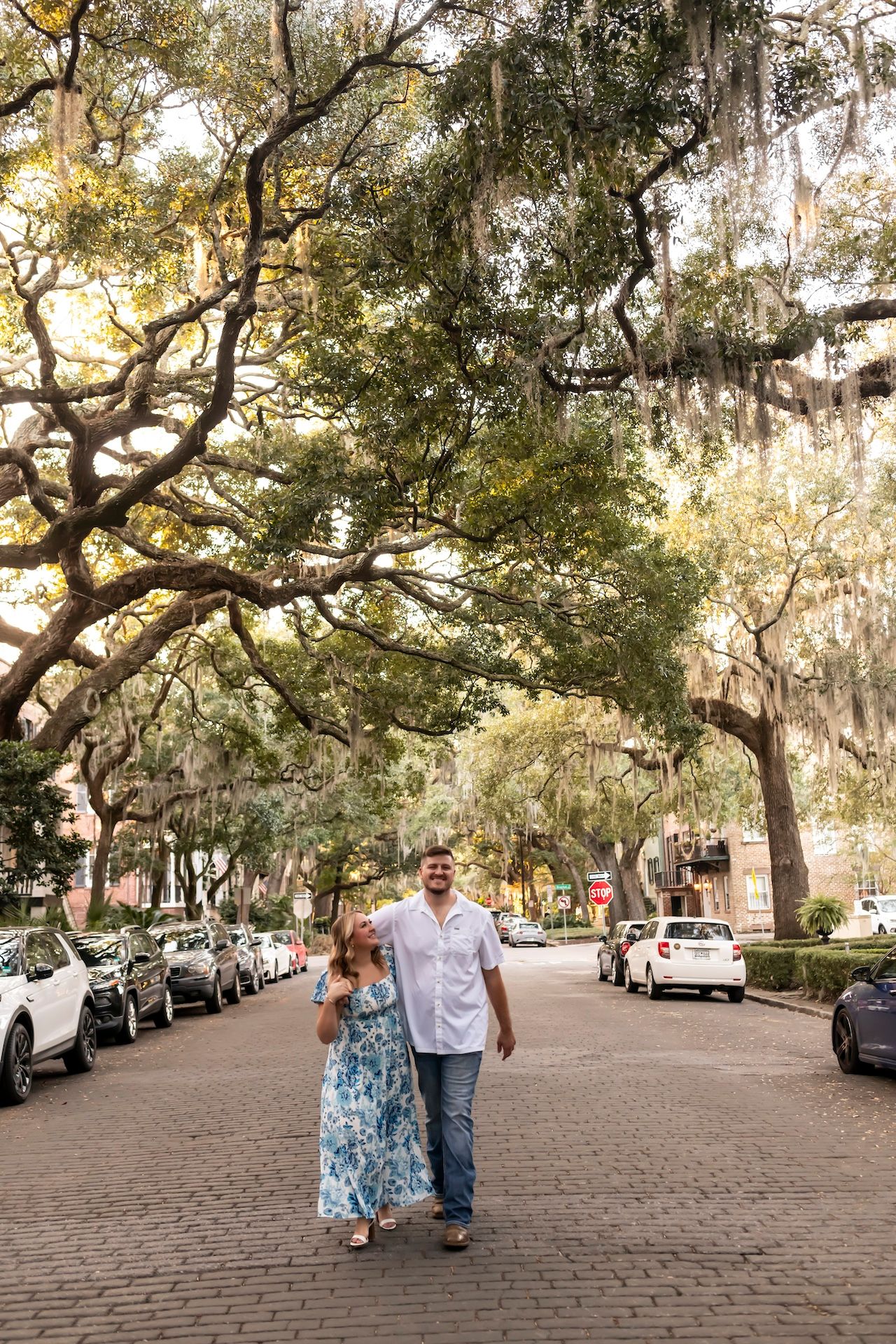 Two people walking together down a charming cobblestone street lined with Spanish moss-draped oak trees in Savannah.