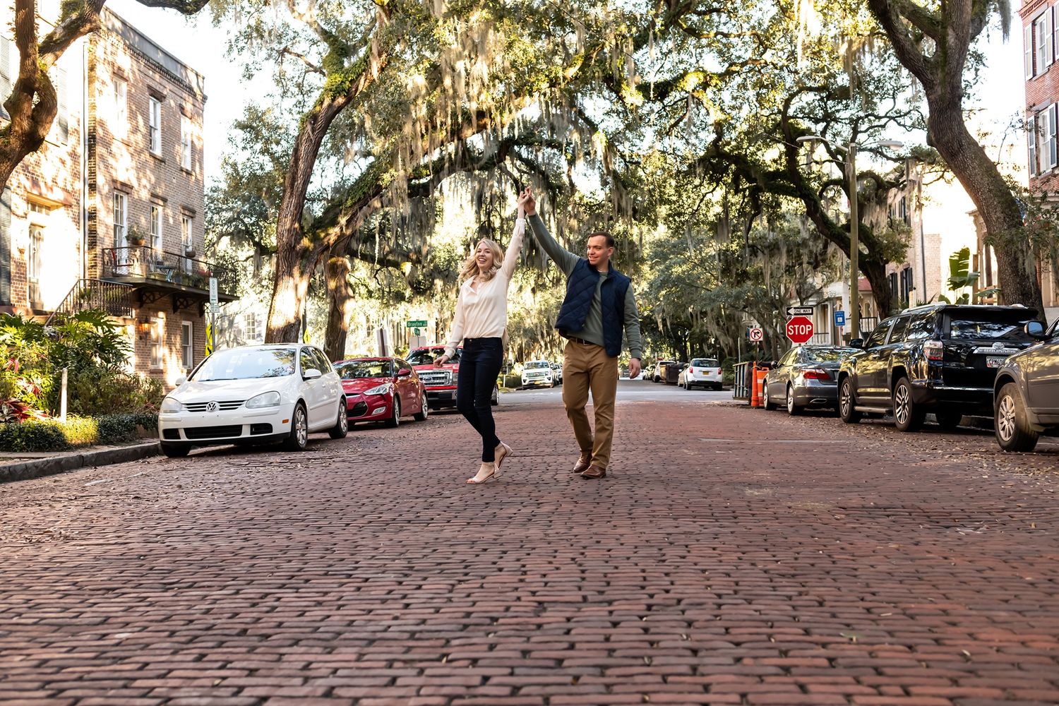 A couple strolls down a cobblestone street lined with Spanish moss-covered trees in historic Savannah, Georgia.