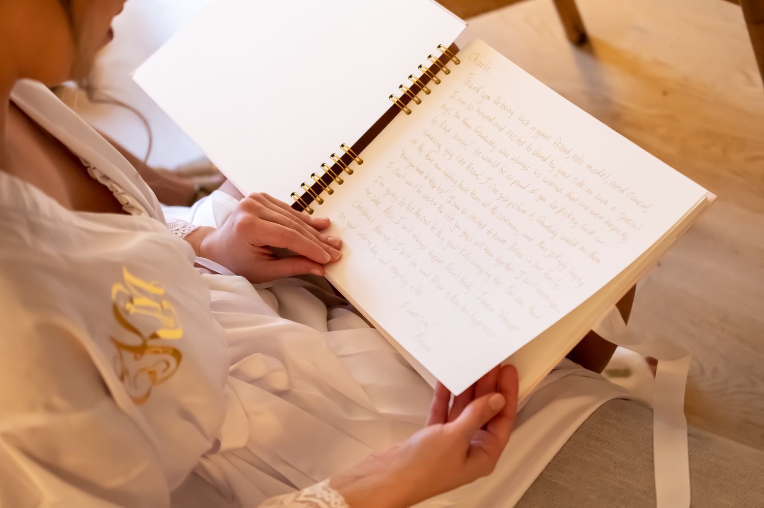 Someone in white clothing writes in a spiral notebook on a wooden surface with crumpled paper nearby.