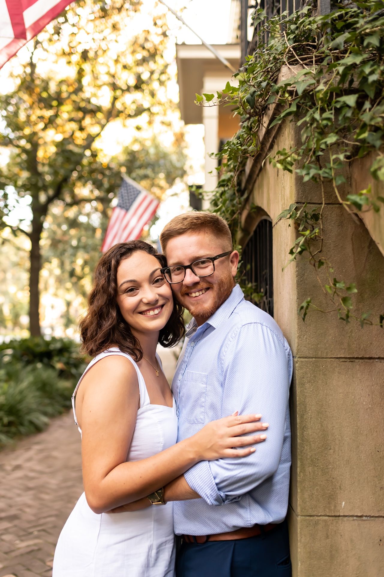 A couple shares a joyful laugh while posing against stone pillars with vines at sunset.