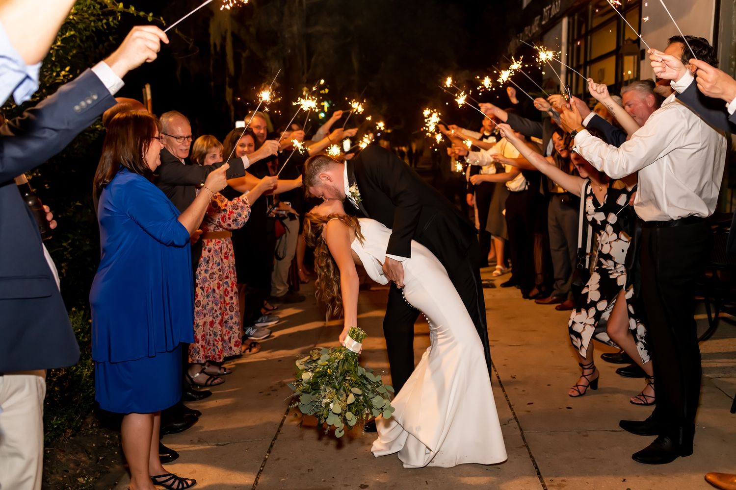 Wedding guests hold sparklers in a line creating a magical walkway for the newlyweds during their evening reception exit.