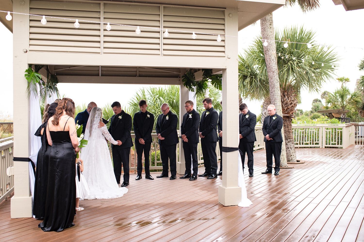 Panoramic view of a wedding ceremony on a covered outdoor deck with palm trees visible in the background.