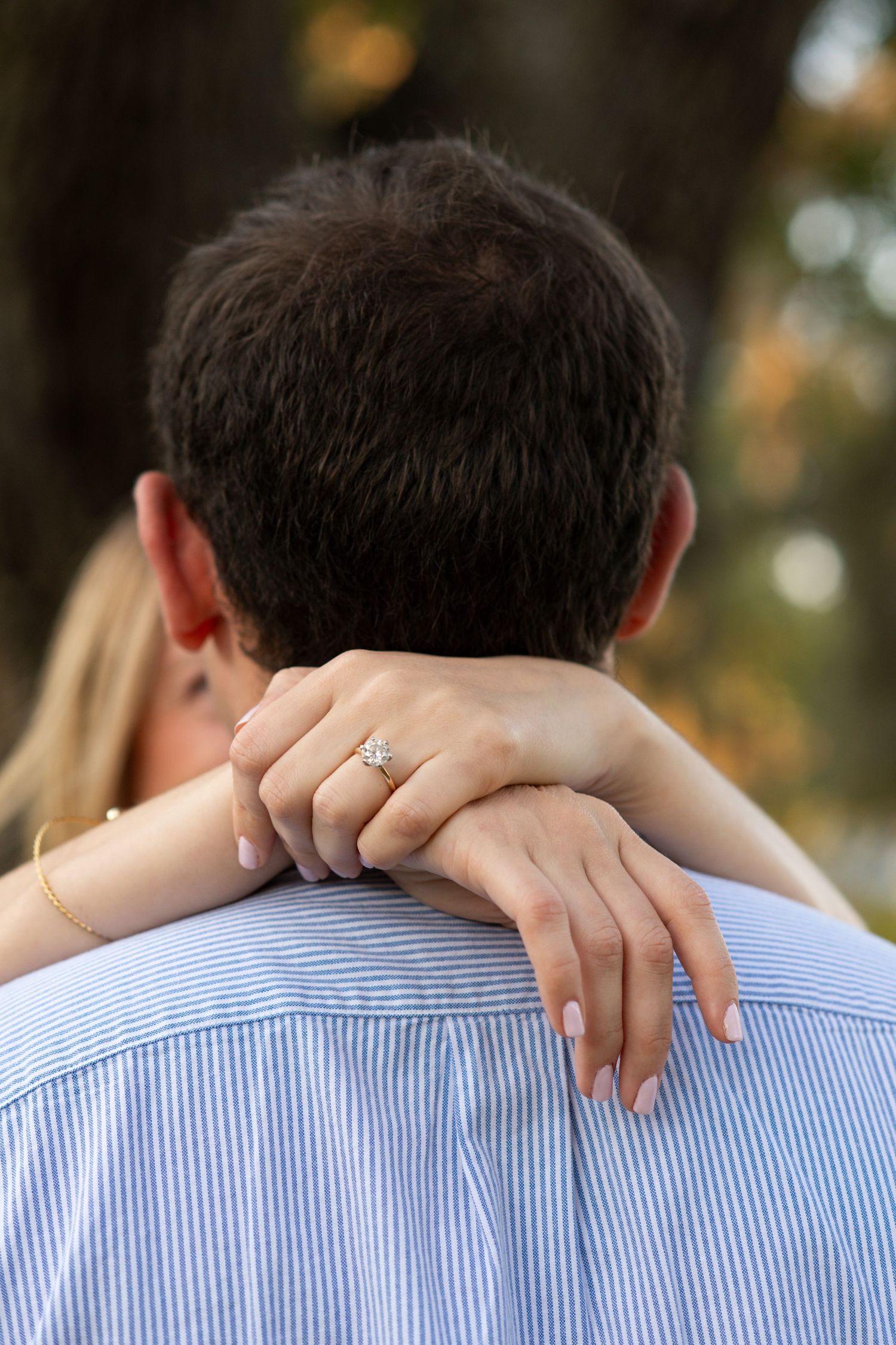 A close-up view of hands embracing shoulders from behind while wearing a blue striped shirt.