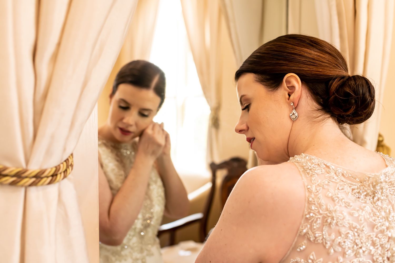 Wedding day preparations with bridal gown and veil being adjusted in soft natural lighting.