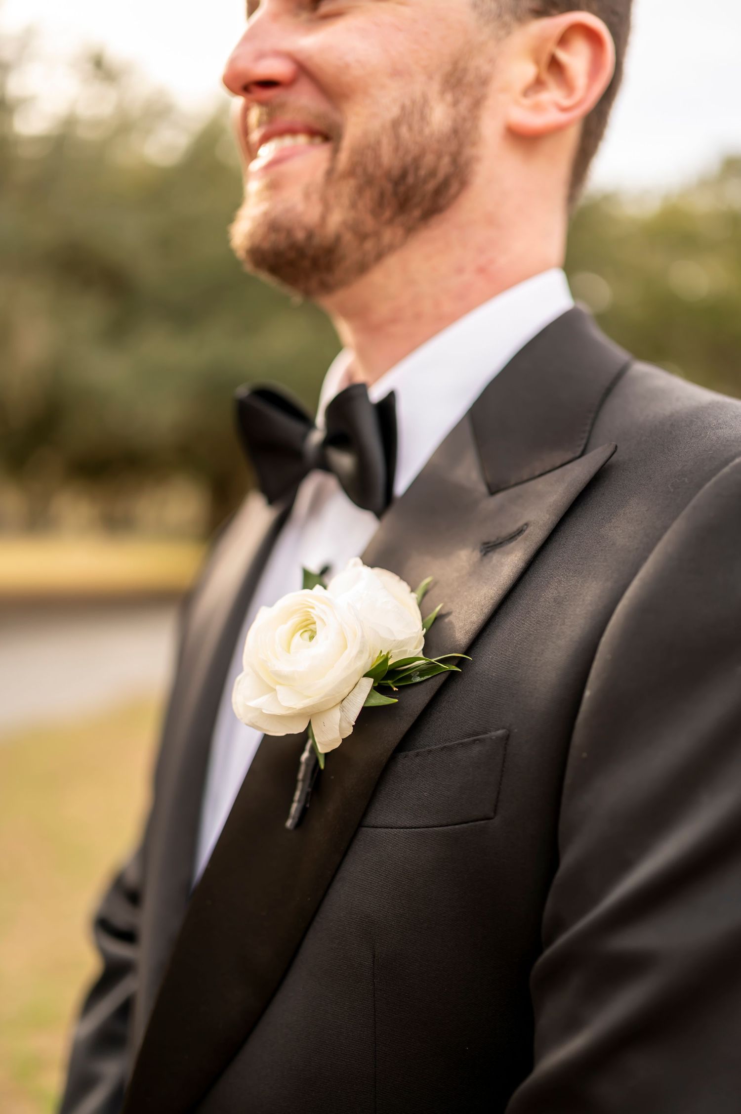 A close-up detail of a groom's elegant white rose boutonniere on a black suit lapel during a special occasion.