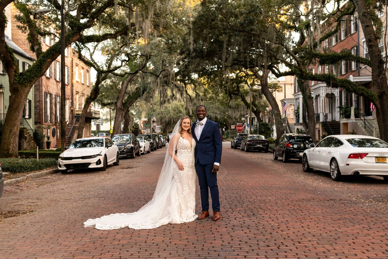 A couple stands on a picturesque brick-paved street lined with oak trees and Spanish moss in Savannah, Georgia.