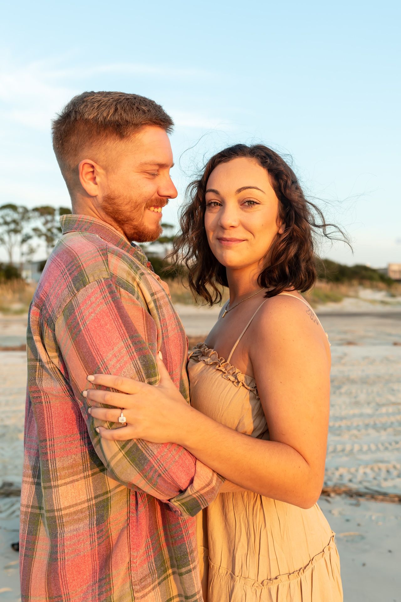 Couple embraces on a beach during golden hour as sunlight creates a warm, romantic glow around them.