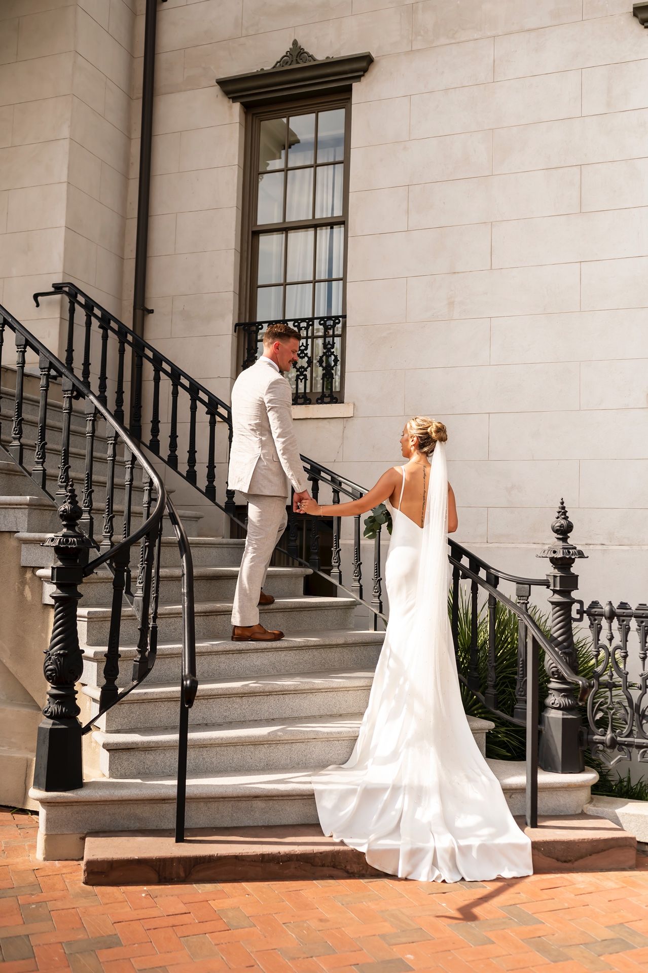 A couple in formal attire poses on historic stone steps with ornate iron railings.