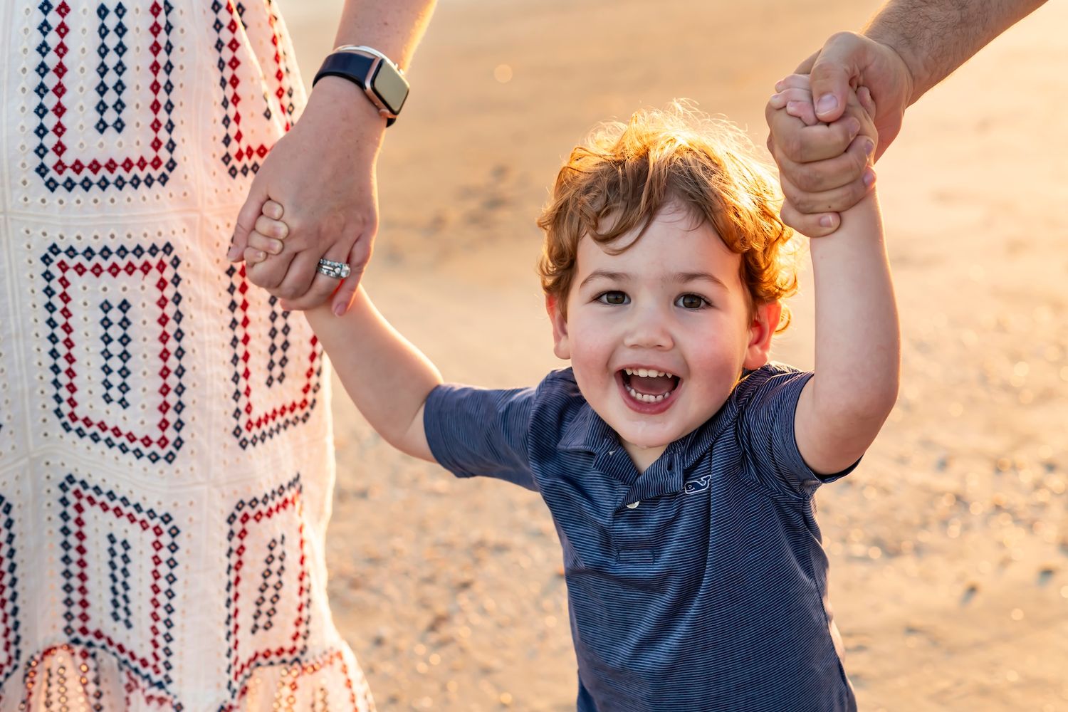 A young child holding hands and laughing with joy on a beach at sunset.