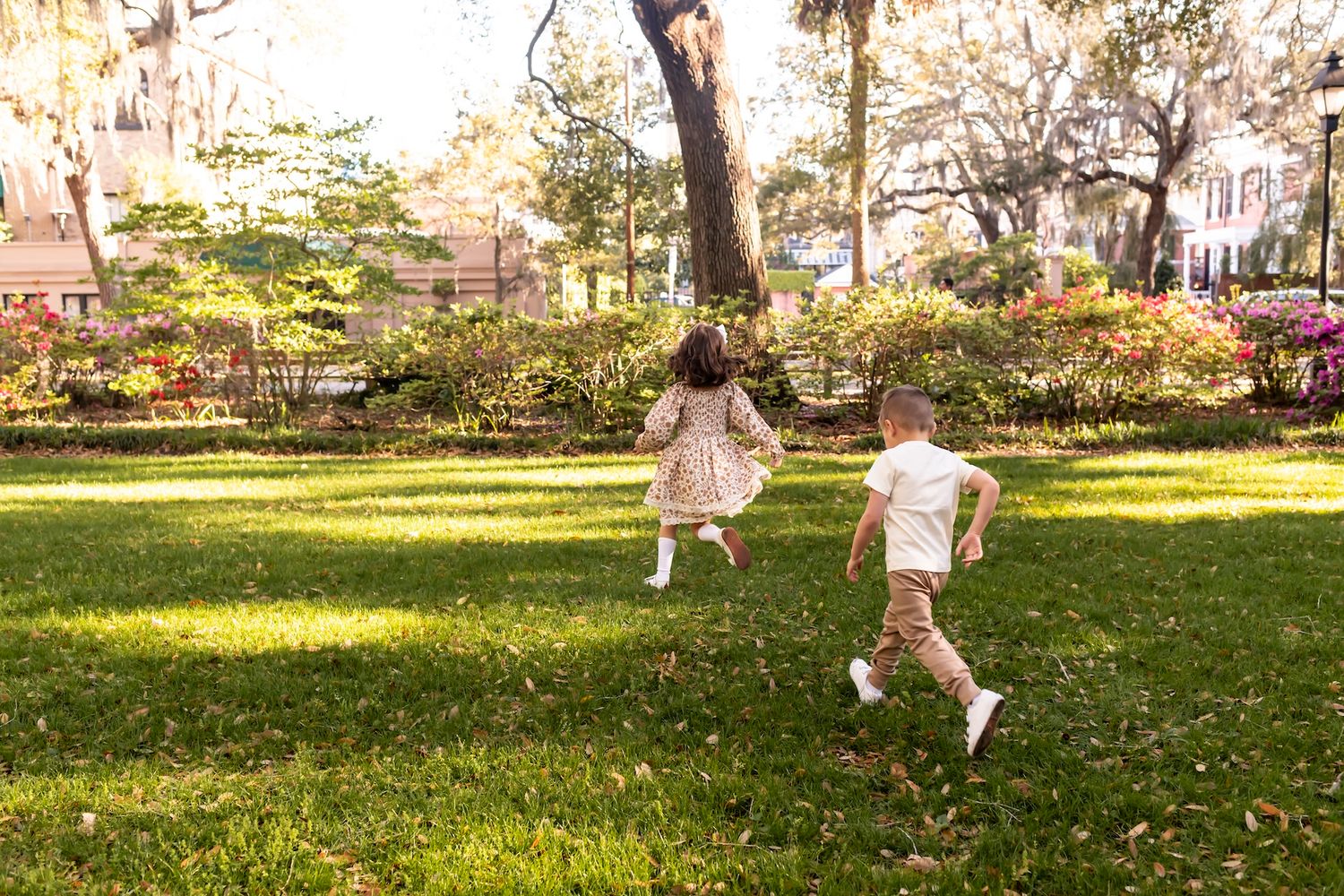 Children play and run together on a sunny lawn in an outdoor park setting during golden hour.