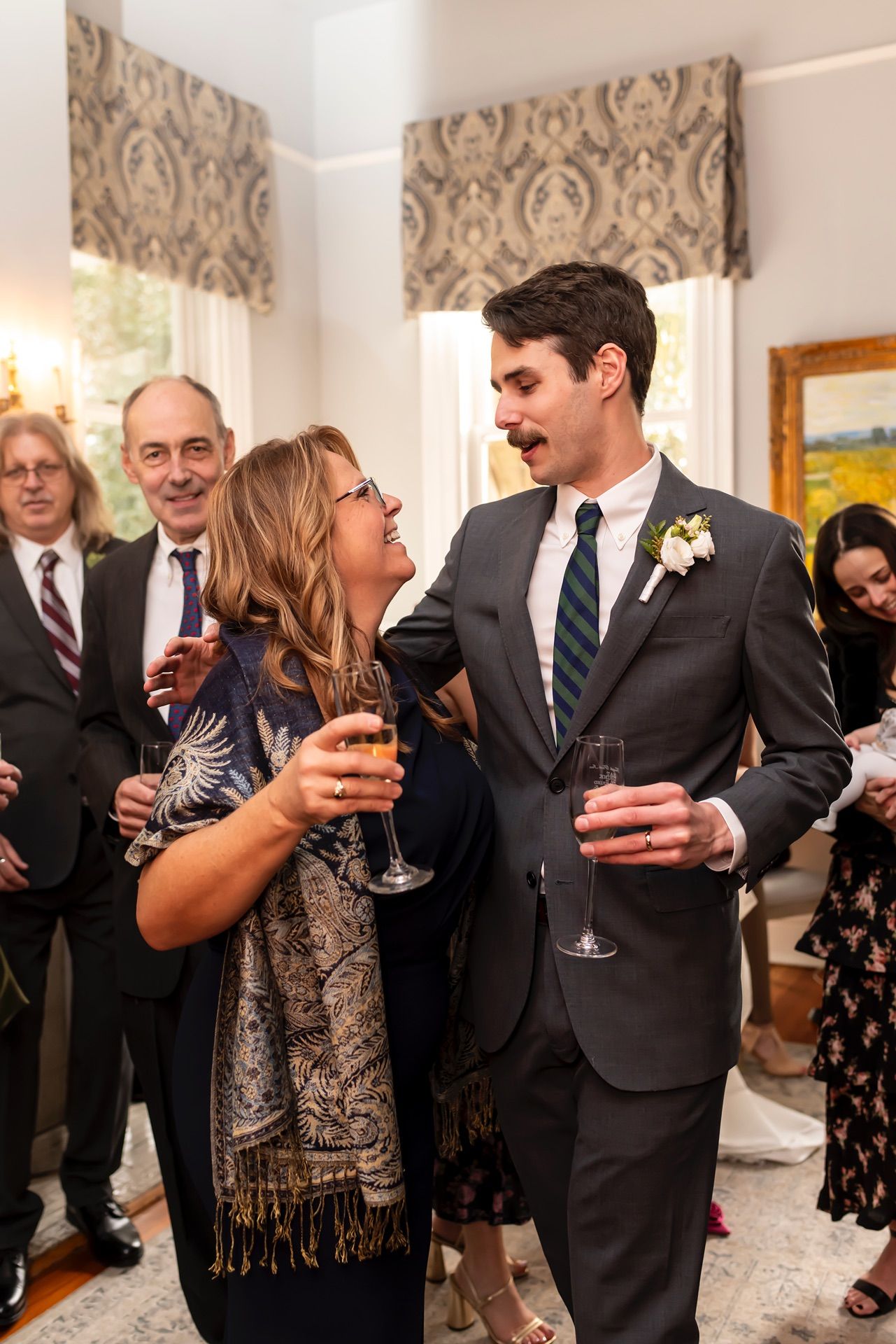Group of elegantly dressed guests mingling and holding wine glasses at an indoor formal celebration party.