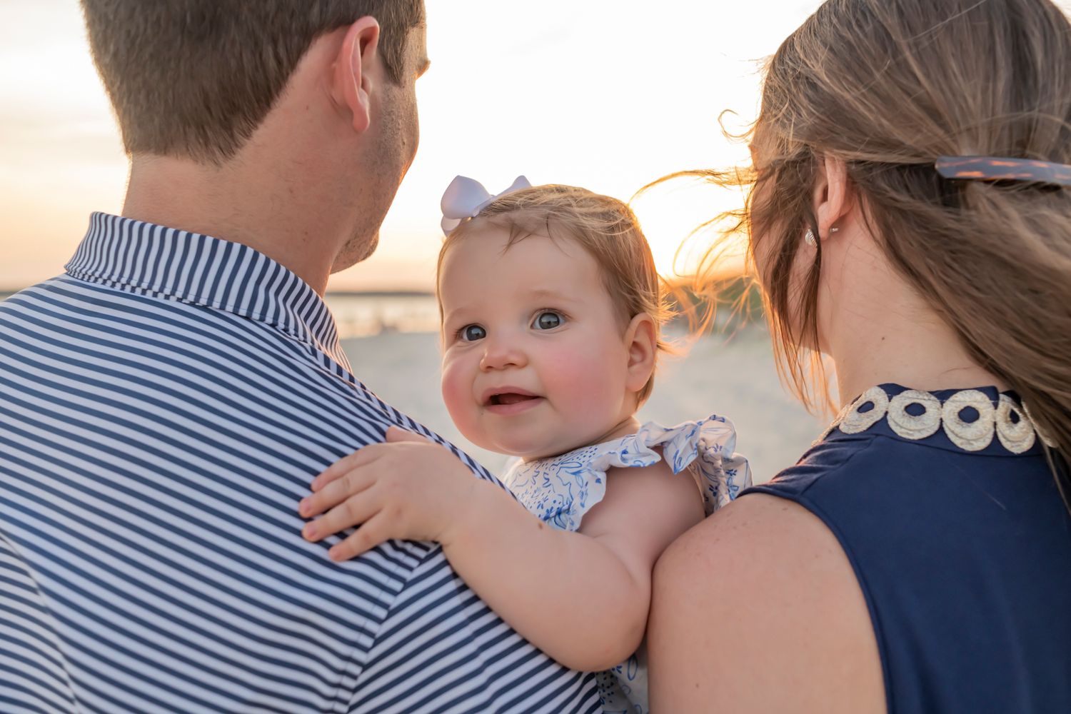 Family embraces on beach during golden sunset wearing coordinated blue and white striped outfits.