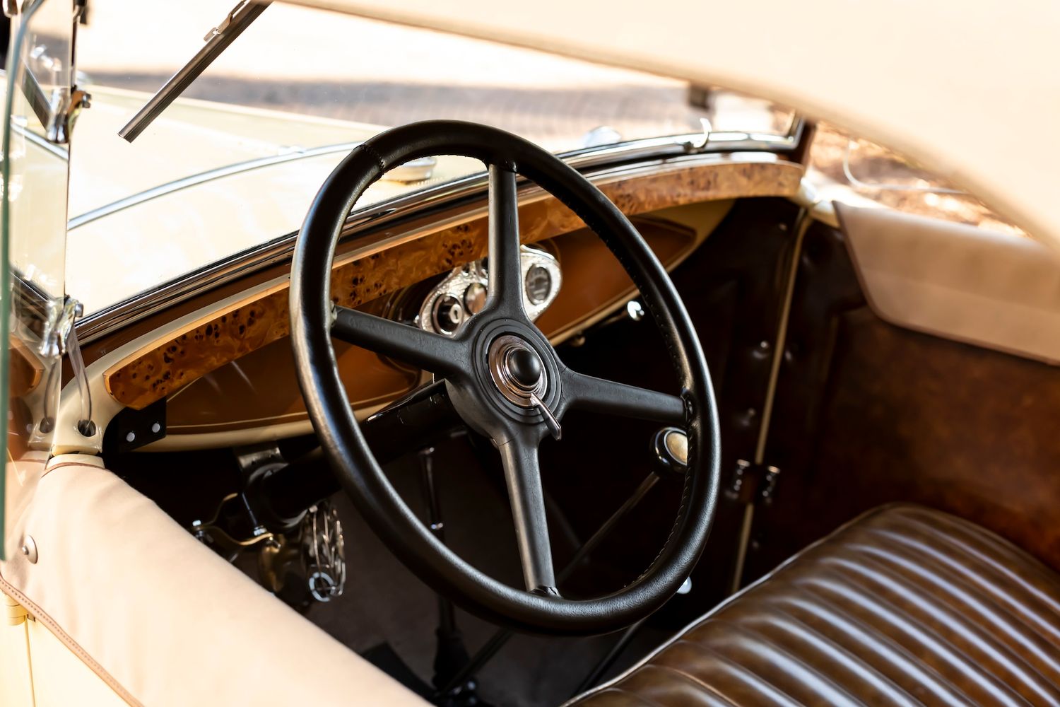 Vintage car interior showing black steering wheel and brown leather bench seat dashboard of classic automobile.