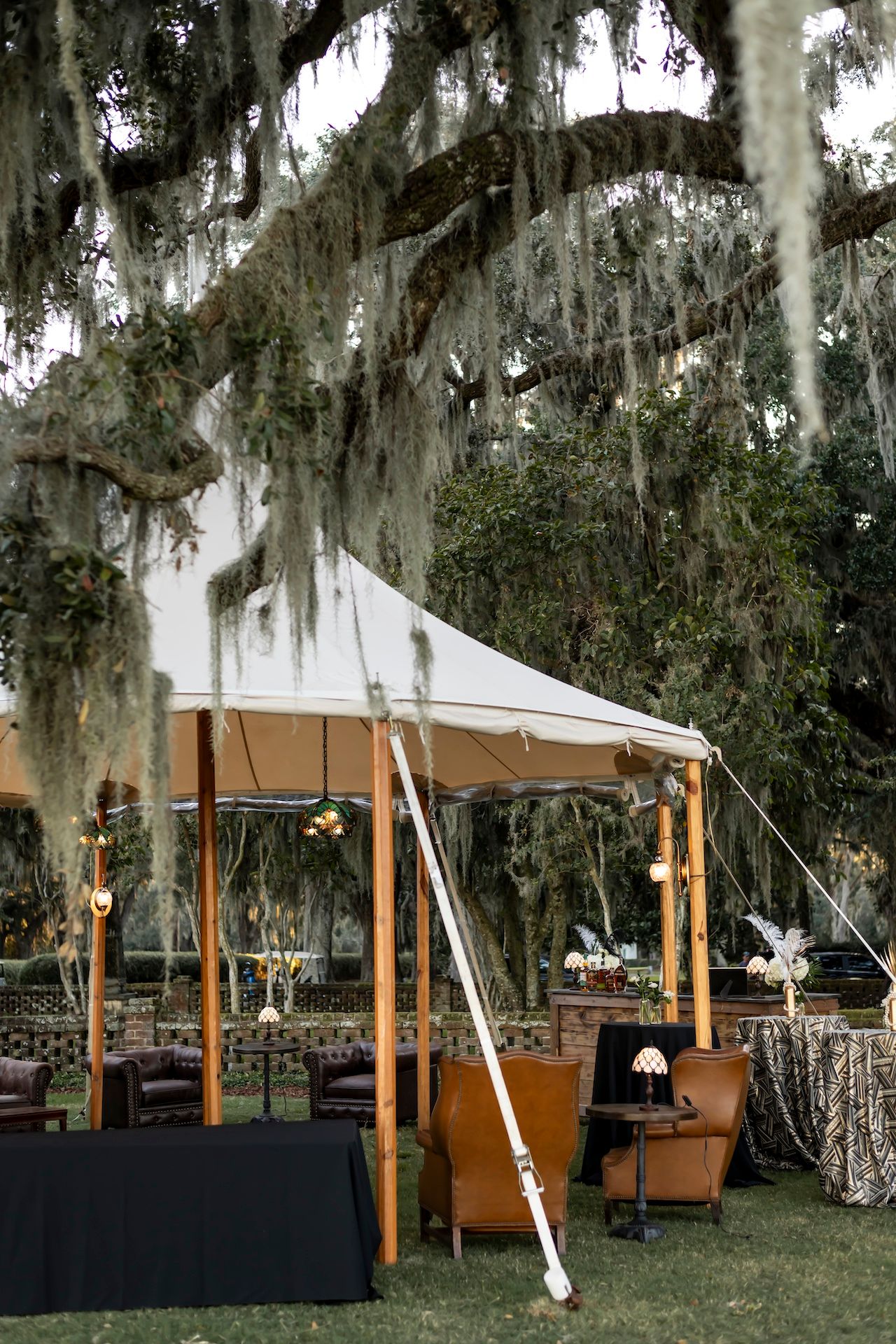 Outdoor event setup with cream-colored tent canopy and Spanish moss draped oak trees creating a romantic atmosphere.